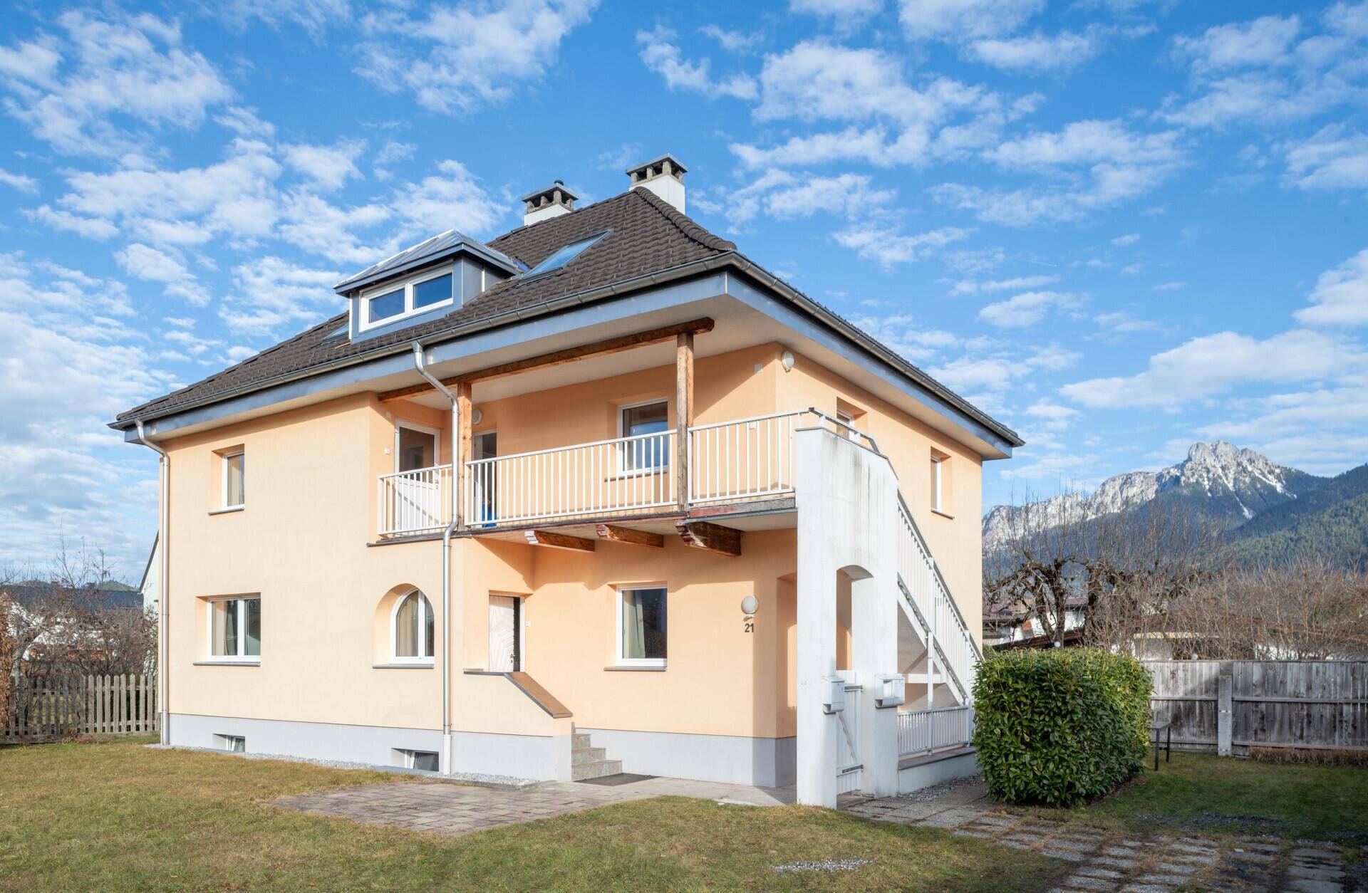 Ansicht des Hauses mit Balkon und Außentreppe, umgeben von Grünflächen und Bergen.