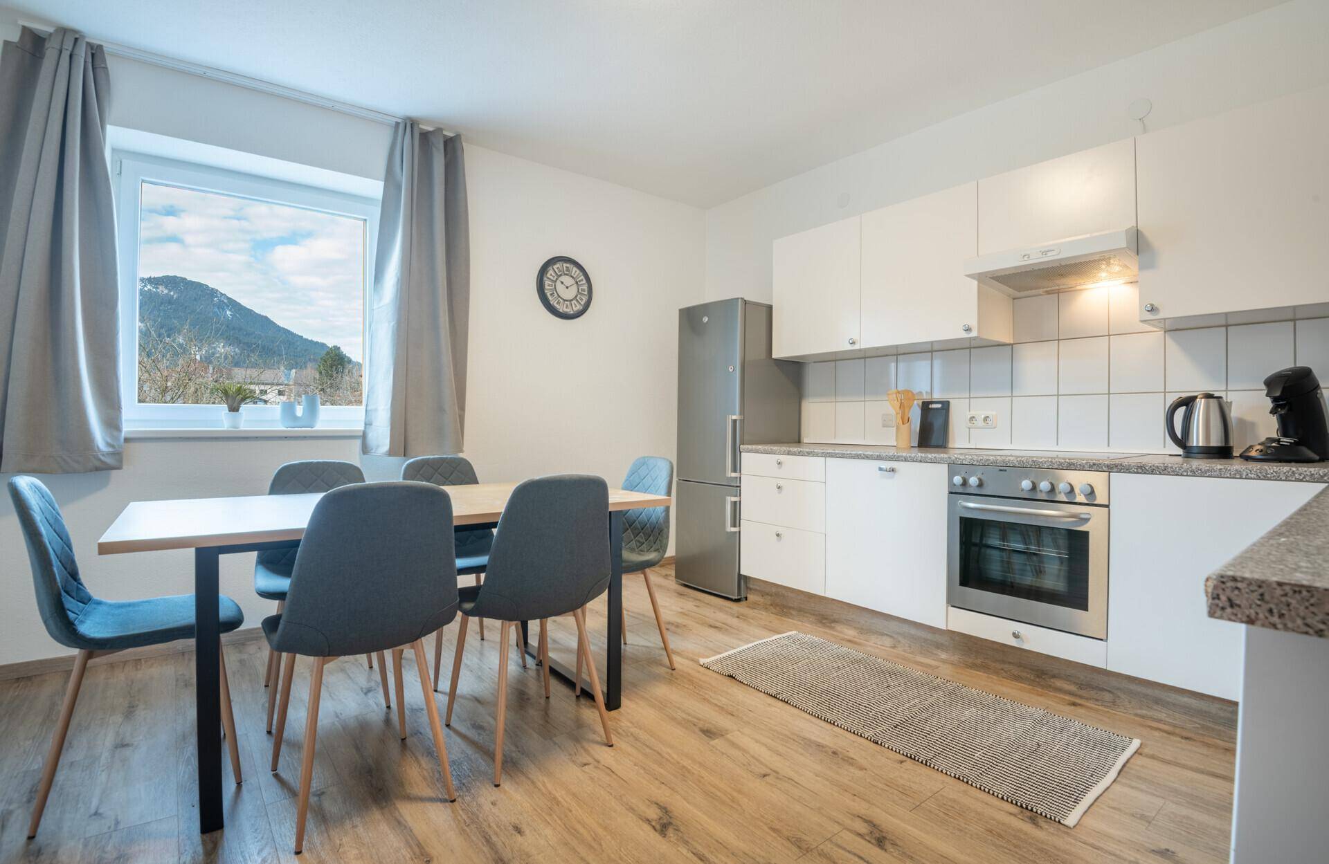 Moderne Wohnküche mit Esstisch, weißen Schränken und Bergblick.