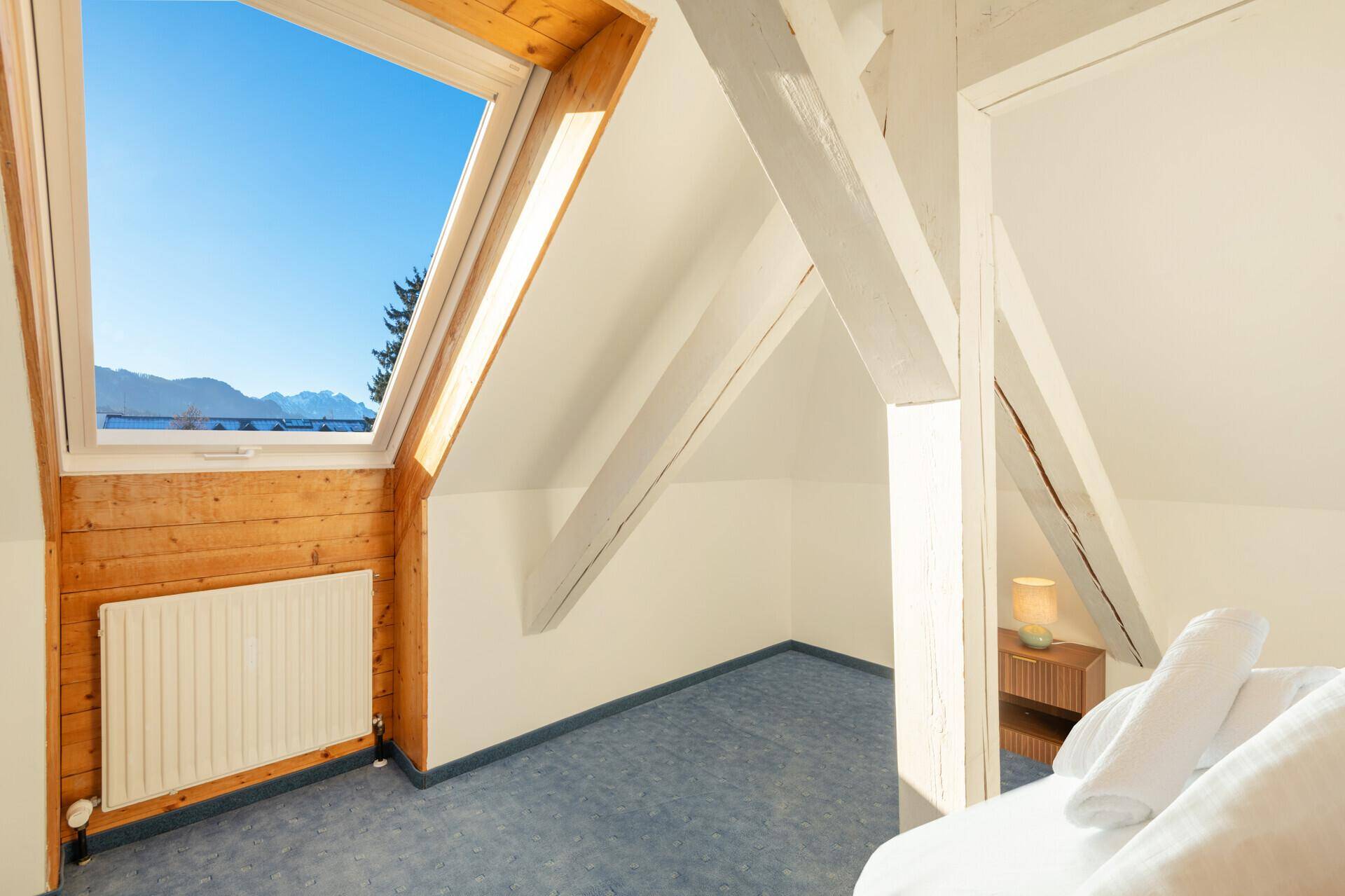 Dachgeschoss-Schlafzimmer mit Holzbalken, Dachfenster und Bergblick.
