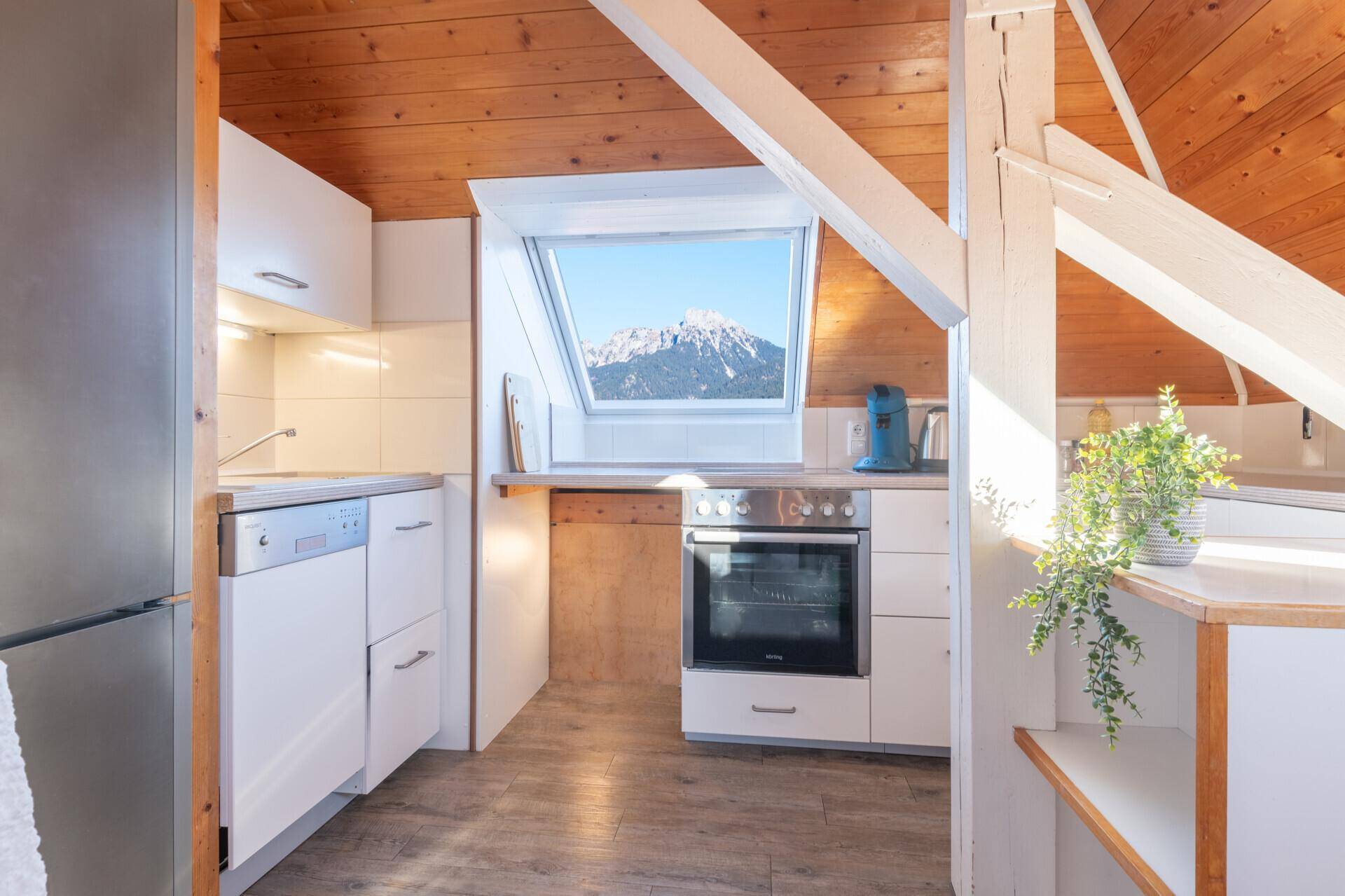 Helle Dachgeschossküche mit Holzwänden, Dachfenster und modernen Geräten.