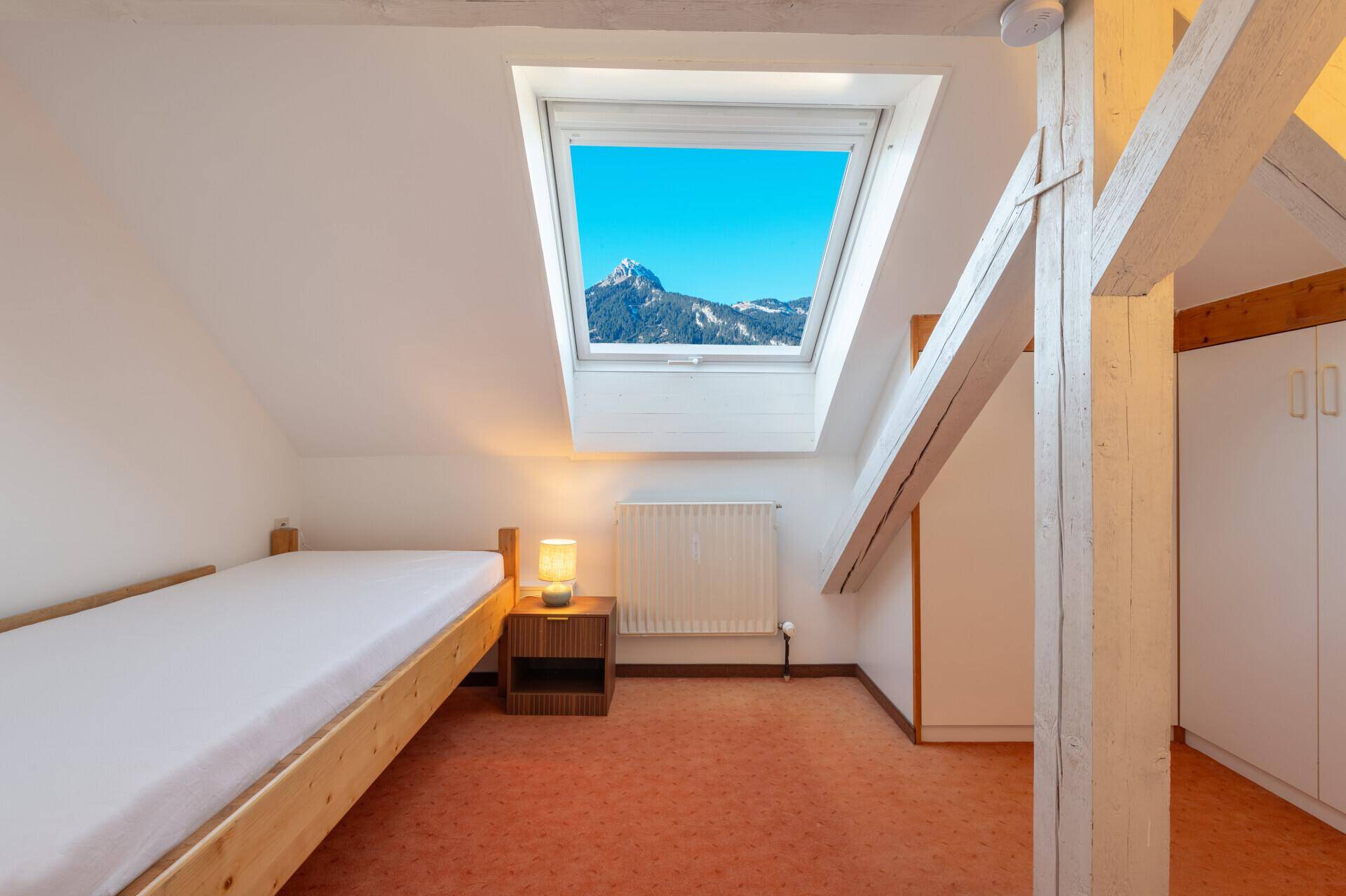 Dachgeschoss-Schlafzimmer mit Holzbalken, Dachfenster und Bergblick.