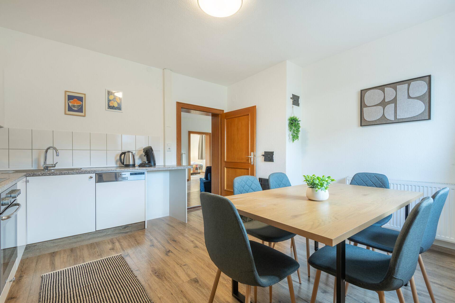 Helle Wohnküche mit Esstisch, weißen Schränken und Zugang zum Flur.