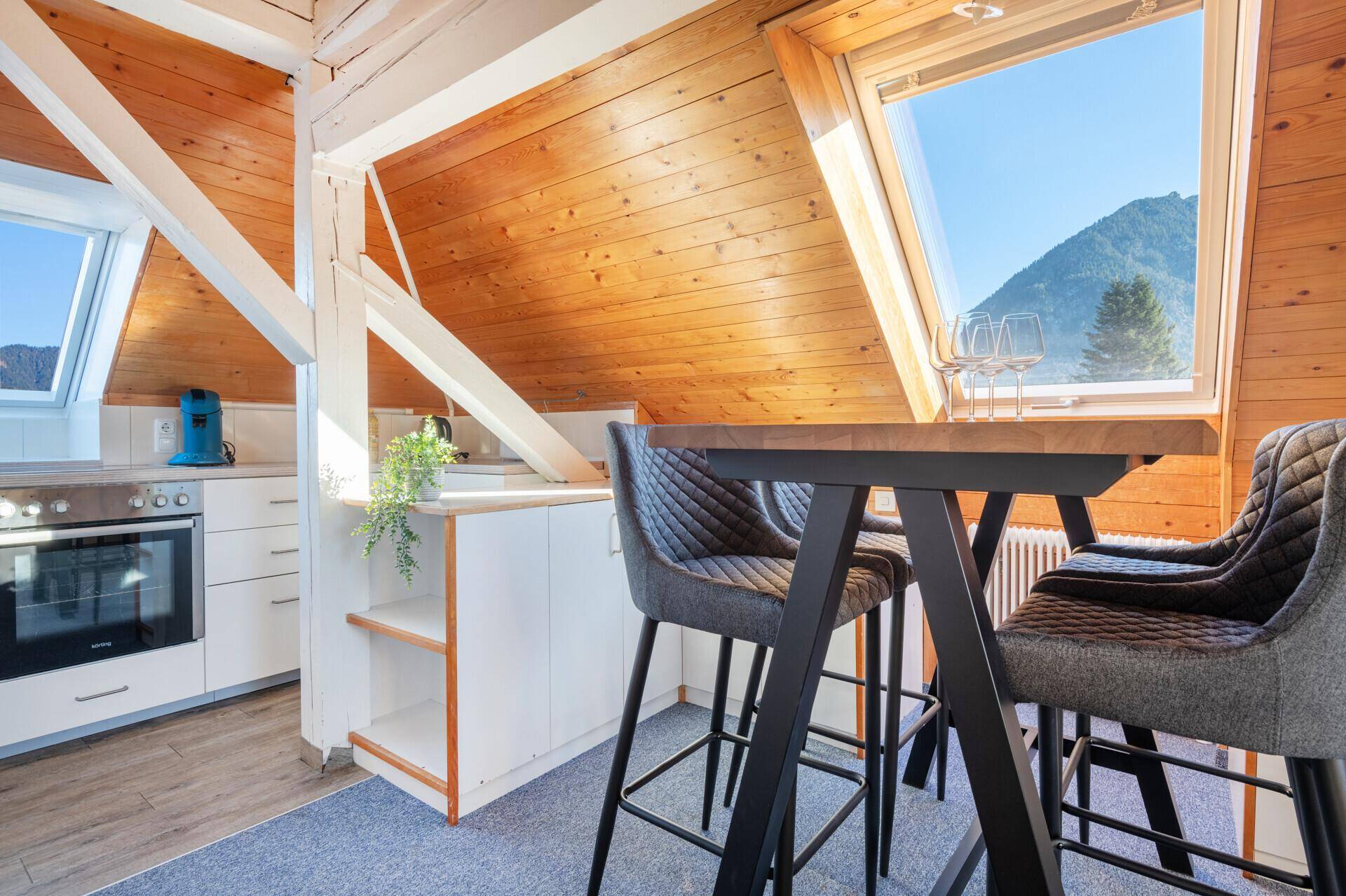 Dachgeschossküche mit Holzwänden, Dachfenster und Barhockern mit Bergblick.