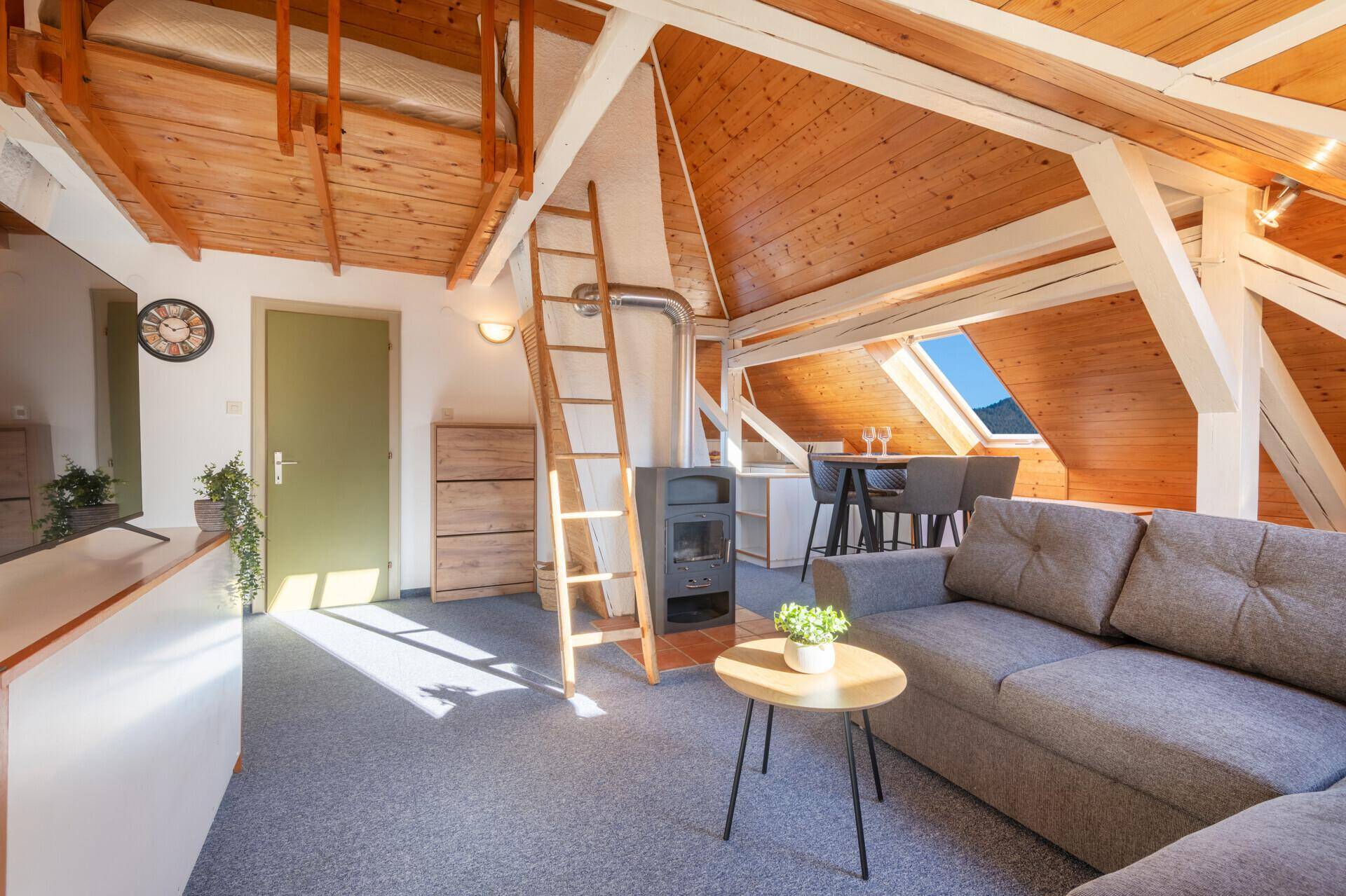 Heller Dachgeschoss-Wohnbereich mit Kaminofen, Holzwänden und Zugang zu einer Empore.