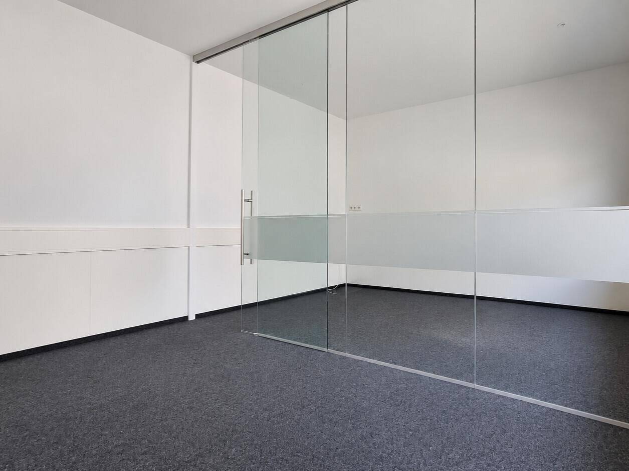 Geräumiger Bürobereich mit Glaswand, Teppichboden und schlichtem, funktionalem Design.