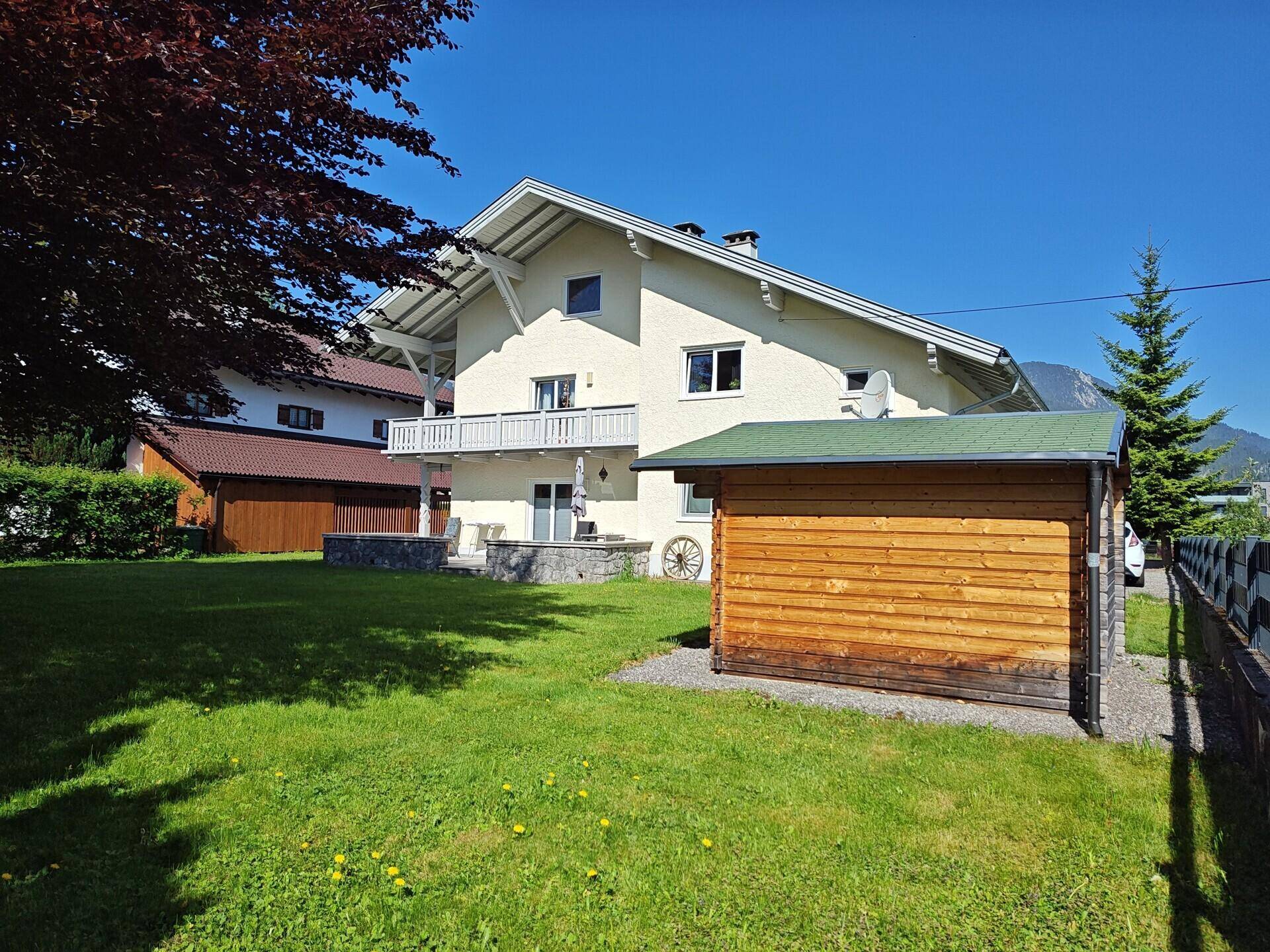 Hinteransicht des Hauses mit gepflegtem Garten, Gartenhaus und Balkon im Obergeschoss.