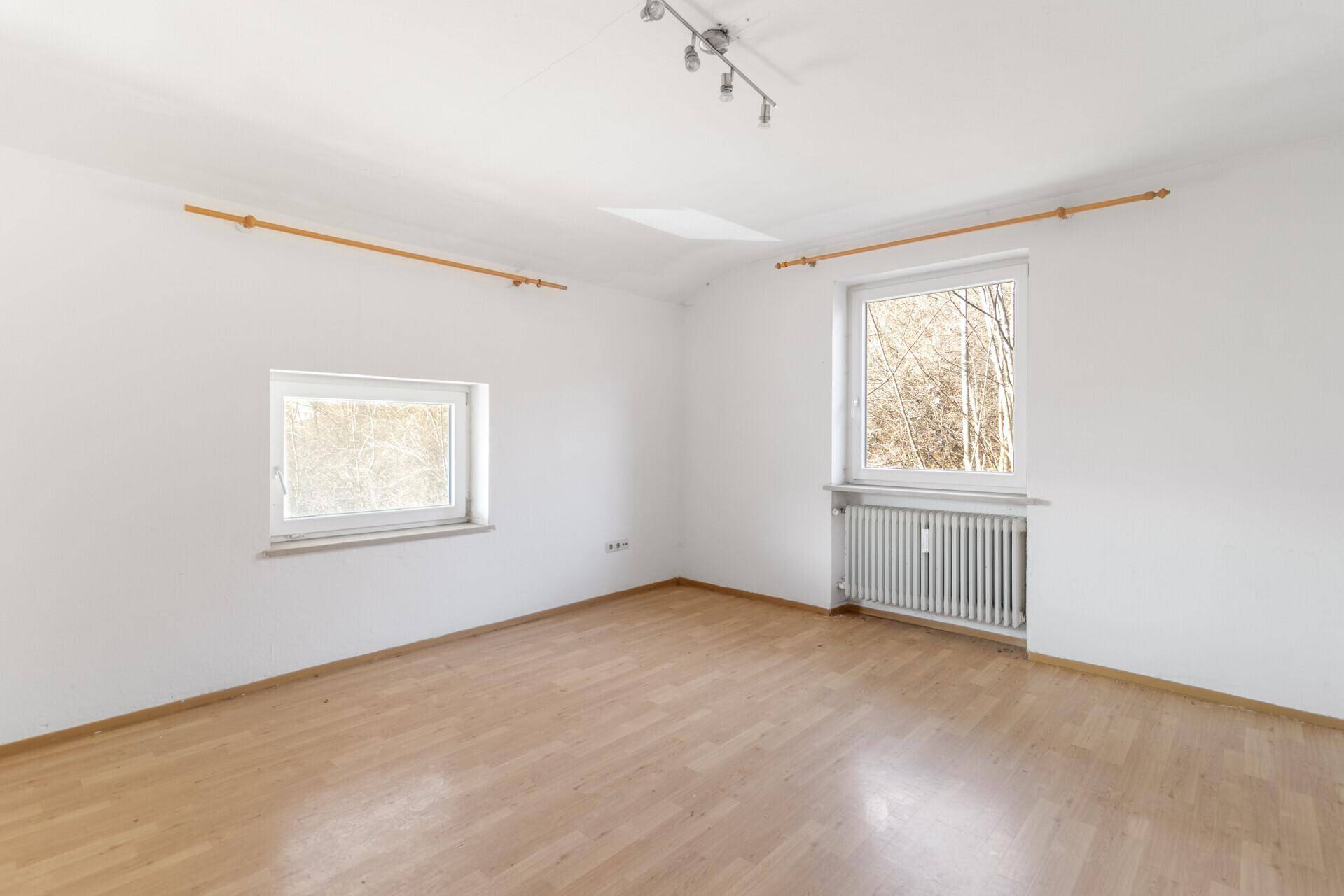Geräumiges Zimmer mit hellem Laminatboden, zwei Fenstern und viel Tageslicht.