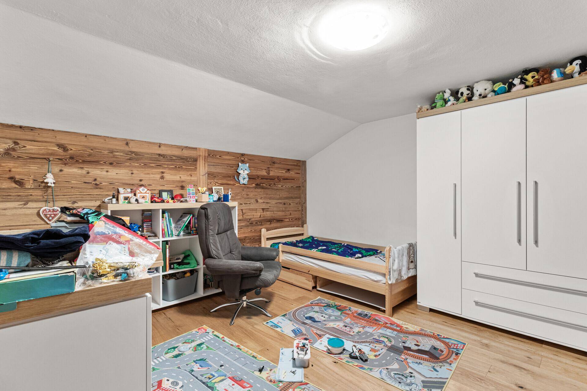 Kinderzimmer mit Holzboden, Holzwand und Spielteppichen, das viel Platz zum Spielen bietet.