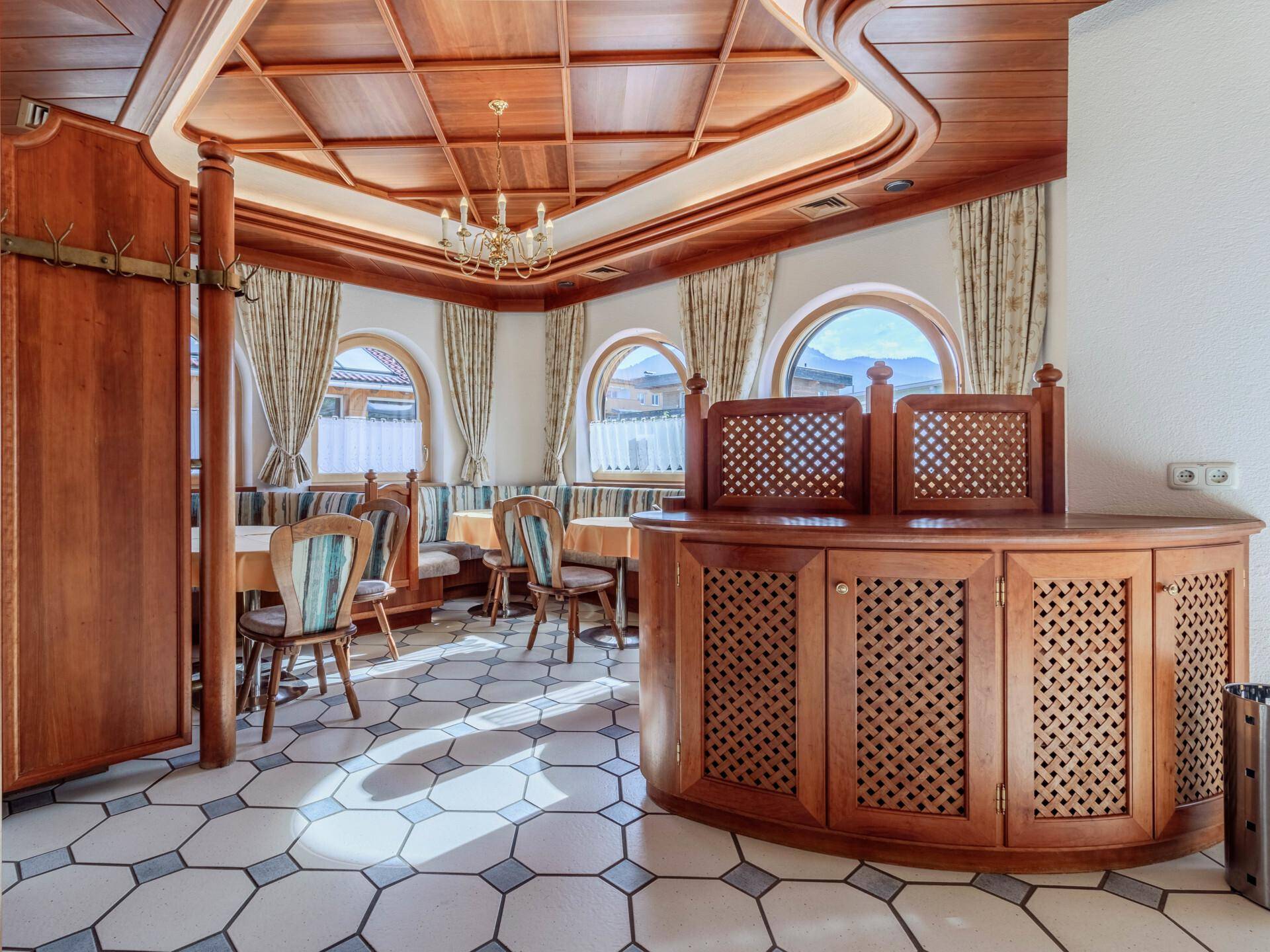 Ein traditioneller Speisesaal mit holzgetäfelten Wänden und Decken, runden Fenstern und gemusterten Fliesen.