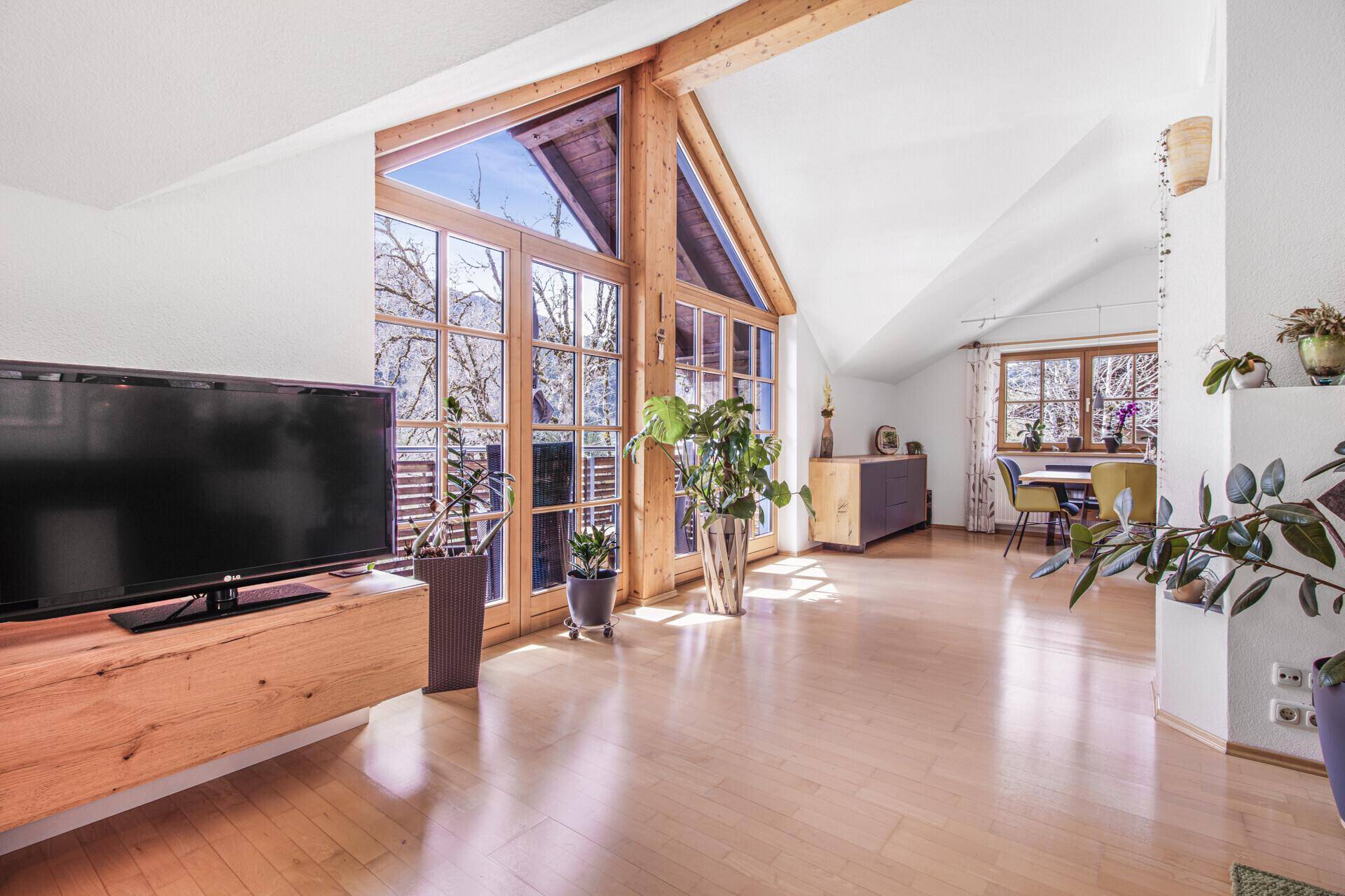 Helles Wohnzimmer mit hohen Decken, Holzbalken und großen Fenstern mit Bergblick.
