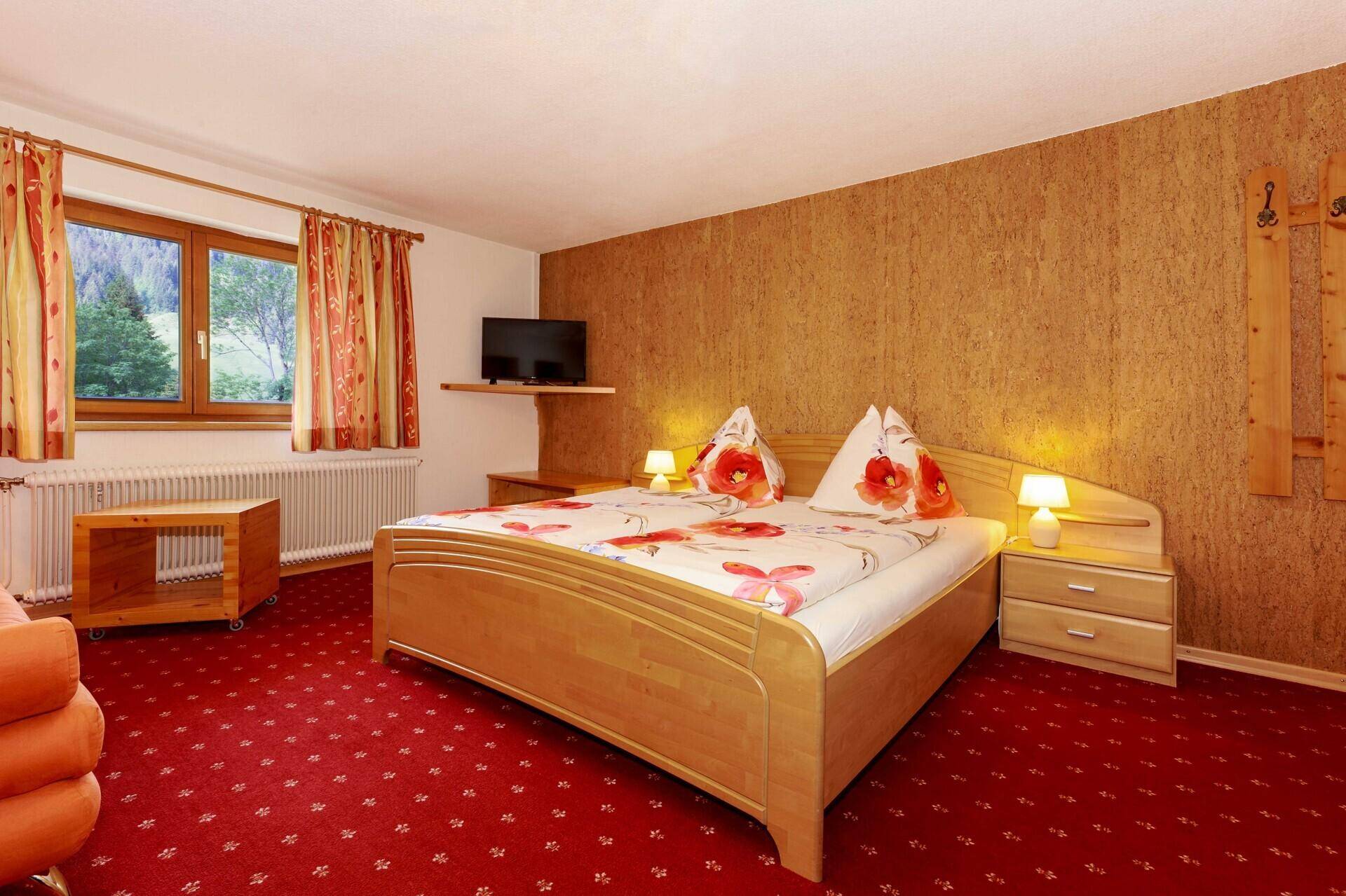 Gemütliches Schlafzimmer mit Holzbett, rotem Teppich und Fenster für Tageslicht.