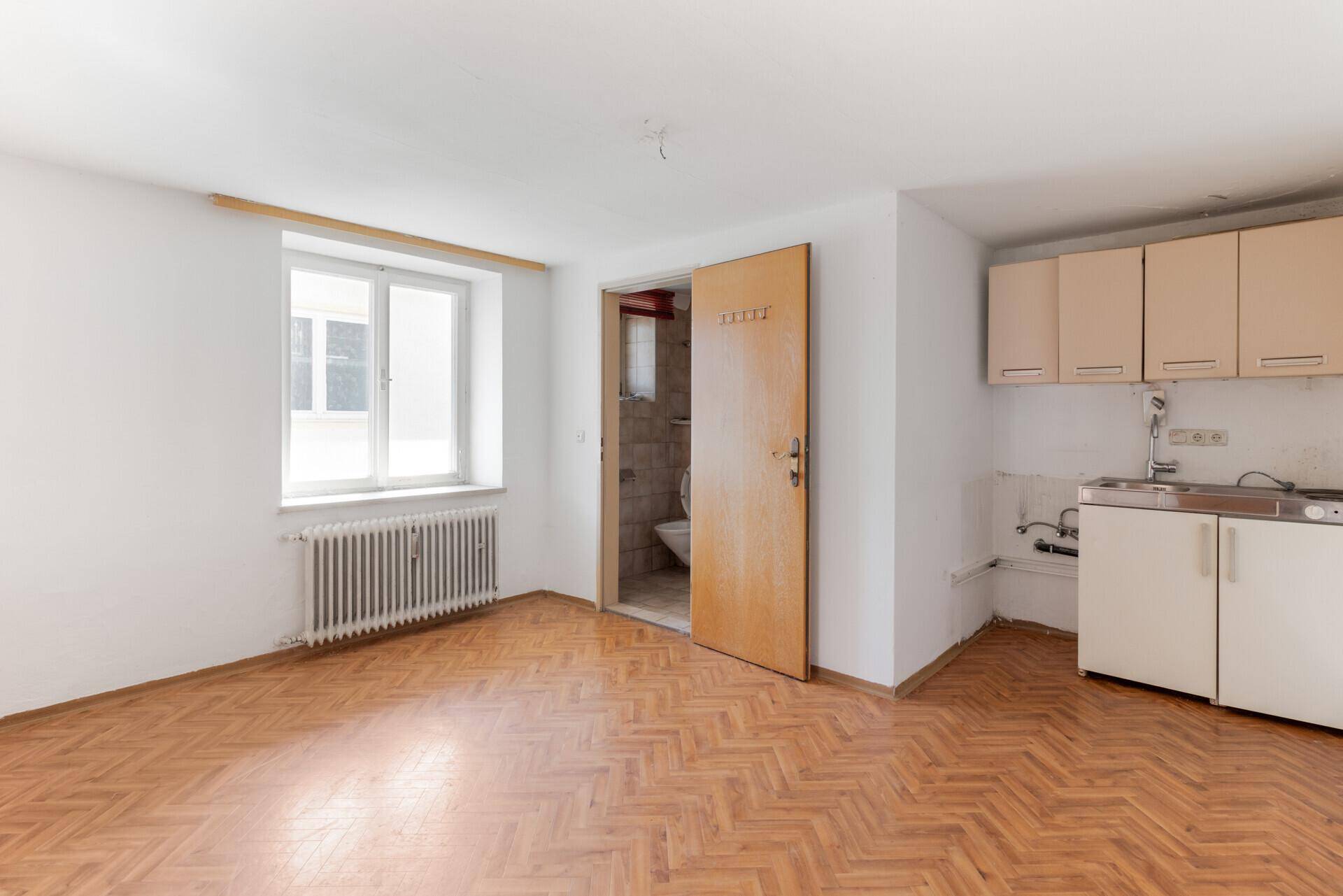 Wohnraum mit Parkettboden, kleiner Küchenzeile und Zugang zu einem separaten WC.