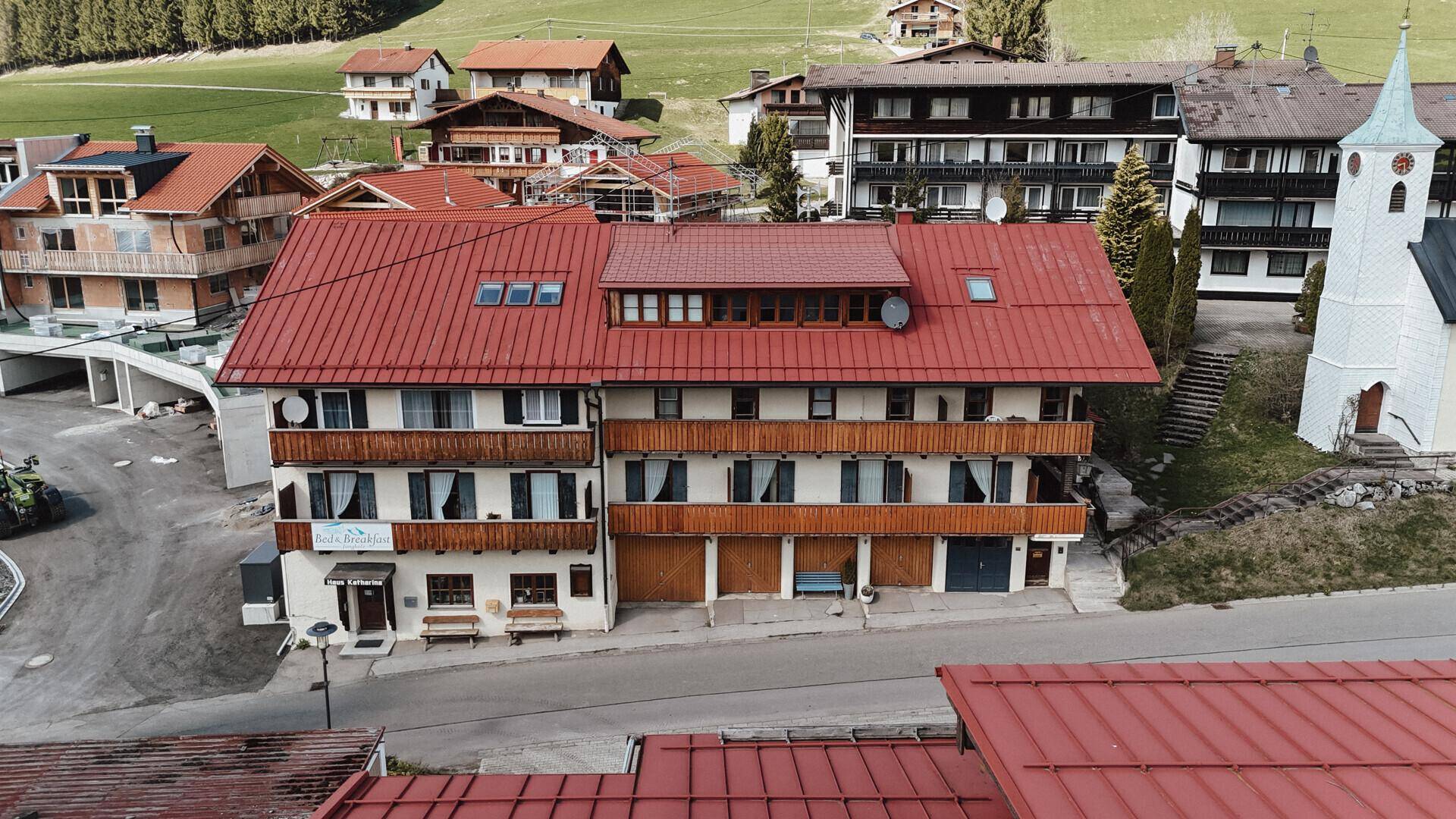 Nahaufnahme eines traditionellen Gebäudes mit rotem Dach, Holzfassade und Balkonen in einer ländlichen Siedlung.