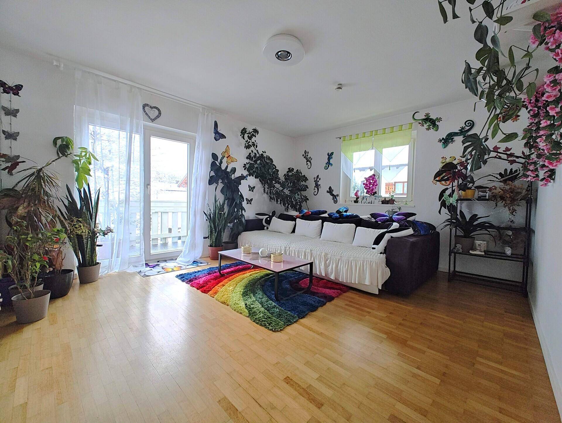 Farbenfrohes Wohnzimmer mit Balkonzugang, vielen Pflanzen und Holzboden.