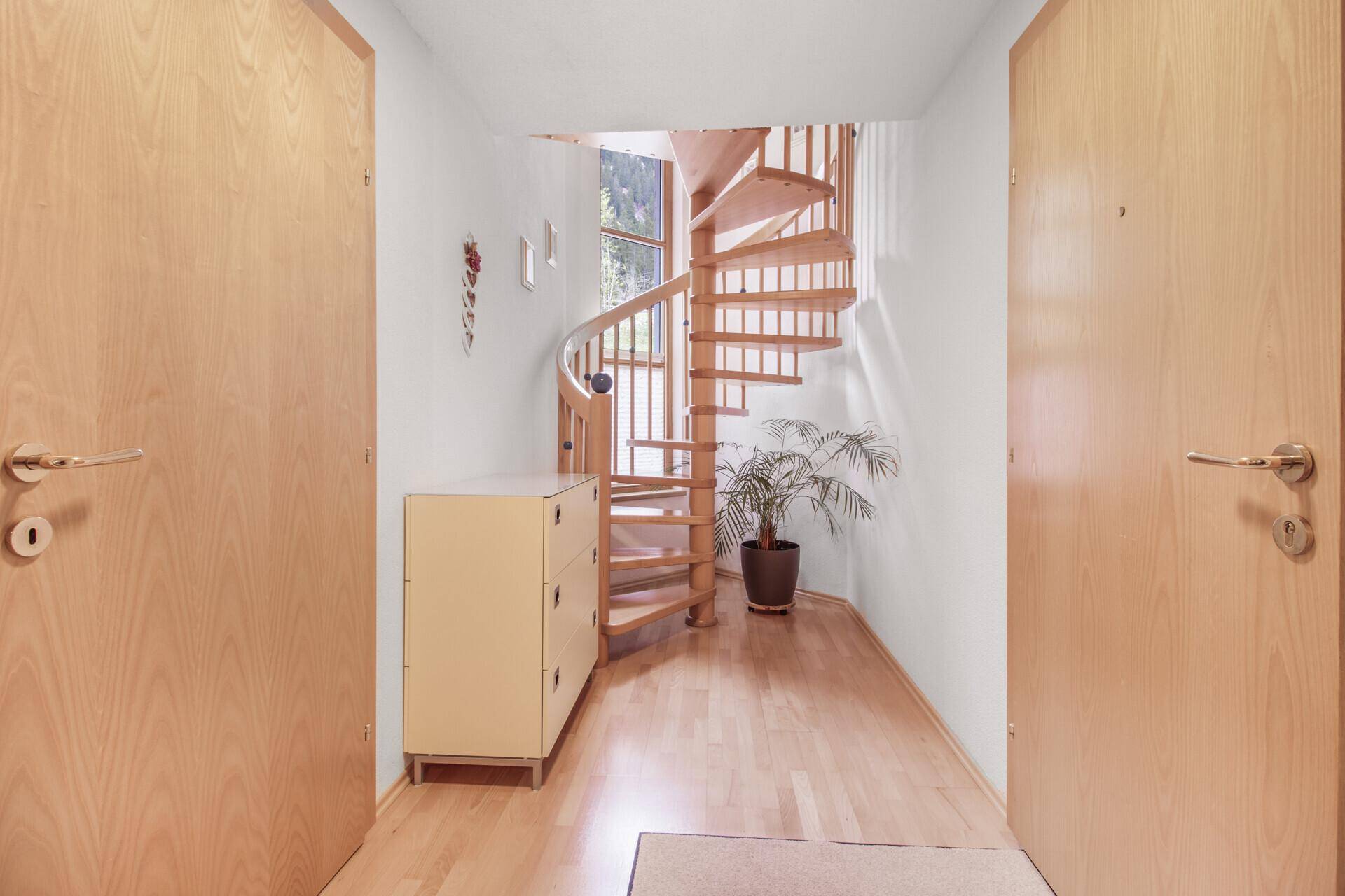 Heller Flur mit eleganter Holzwendeltreppe und praktischem Stauraum.