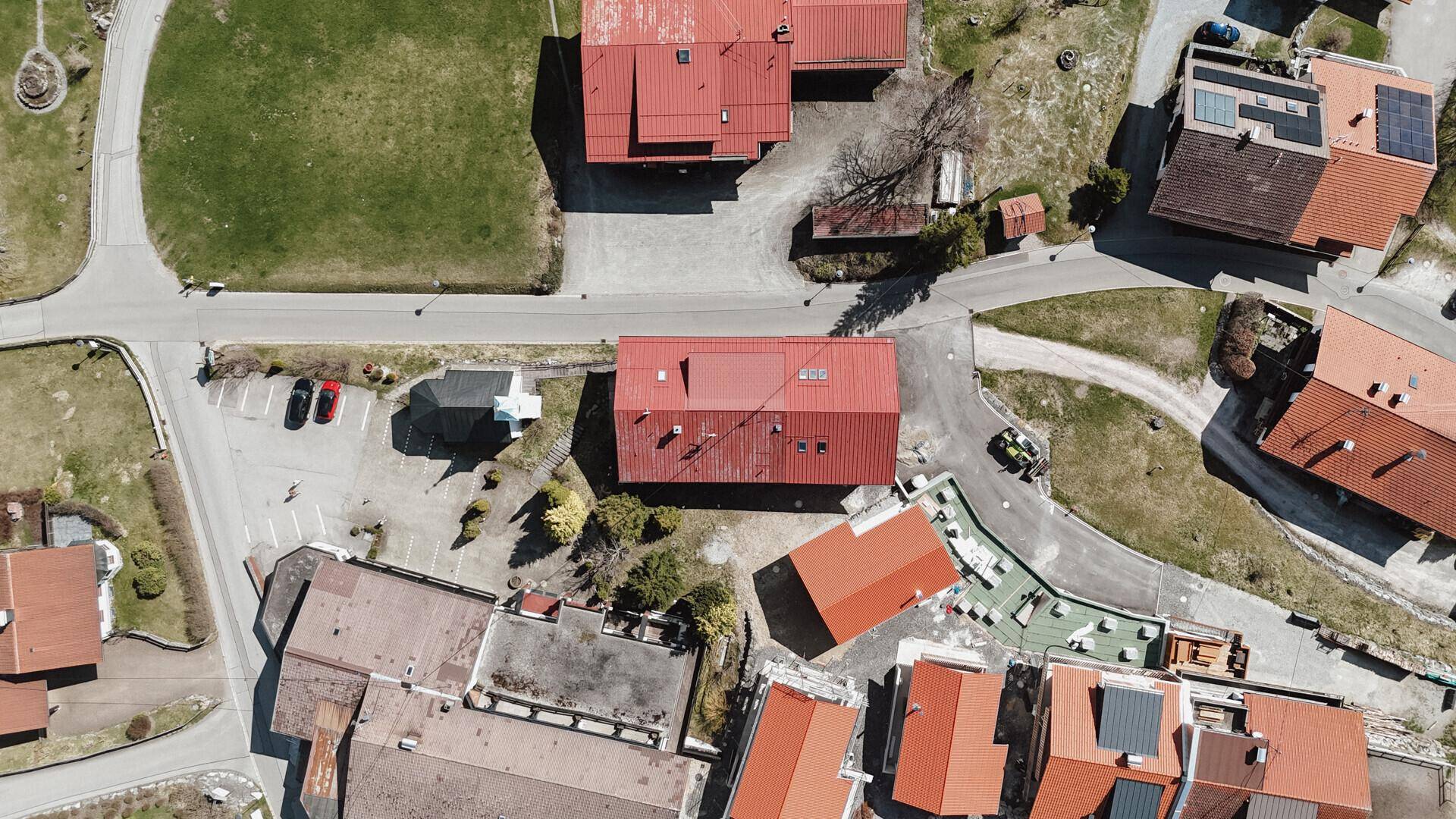 Luftaufnahme von oben zeigt das Gebäude mit rotem Dach und die umliegende Bebauung sowie Parkplätze.