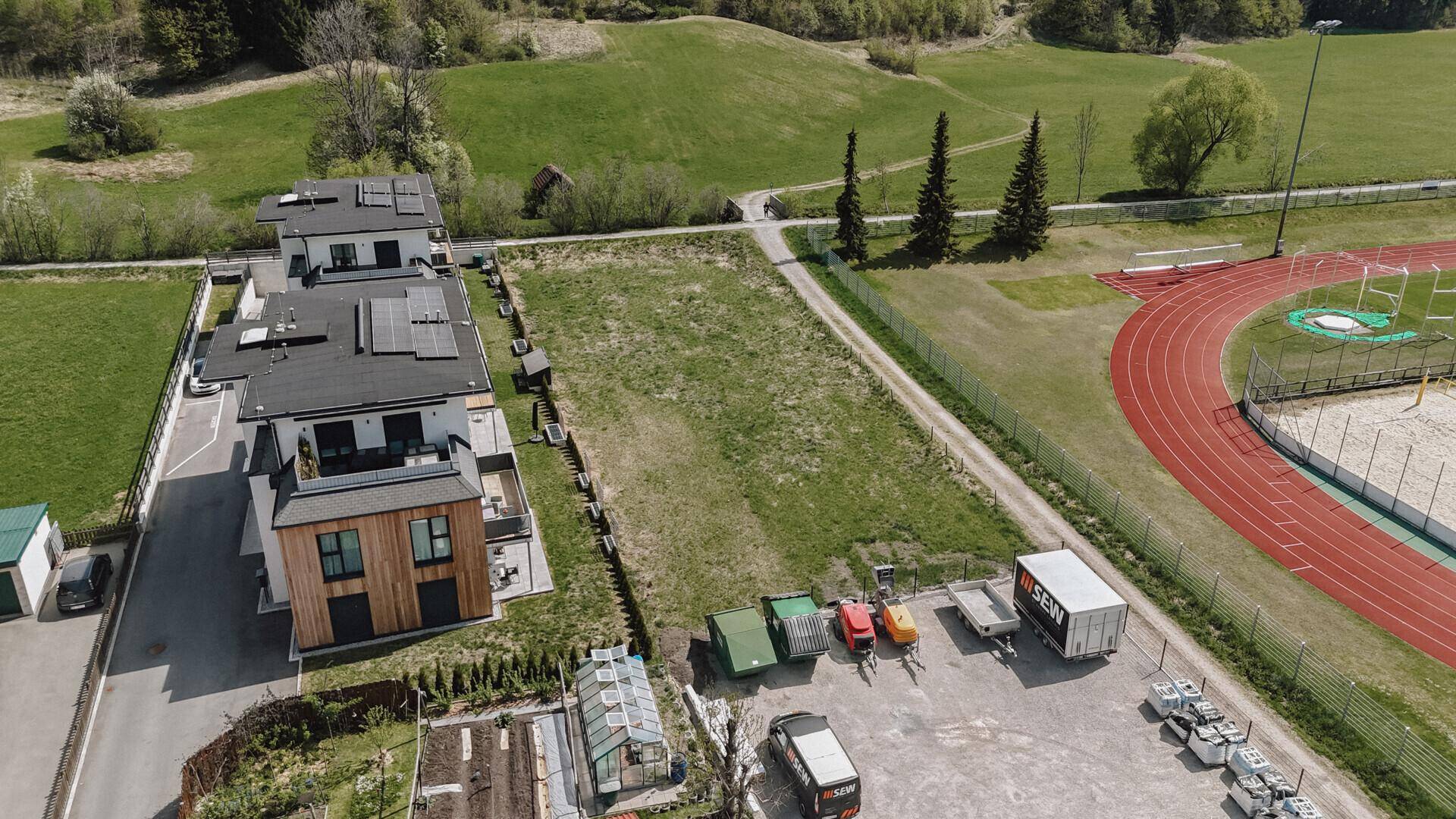 Luftaufnahme eines modernen Gebäudes mit Solaranlage auf dem Dach, angrenzend an ein grünes Grundstück und Sportanlagen.