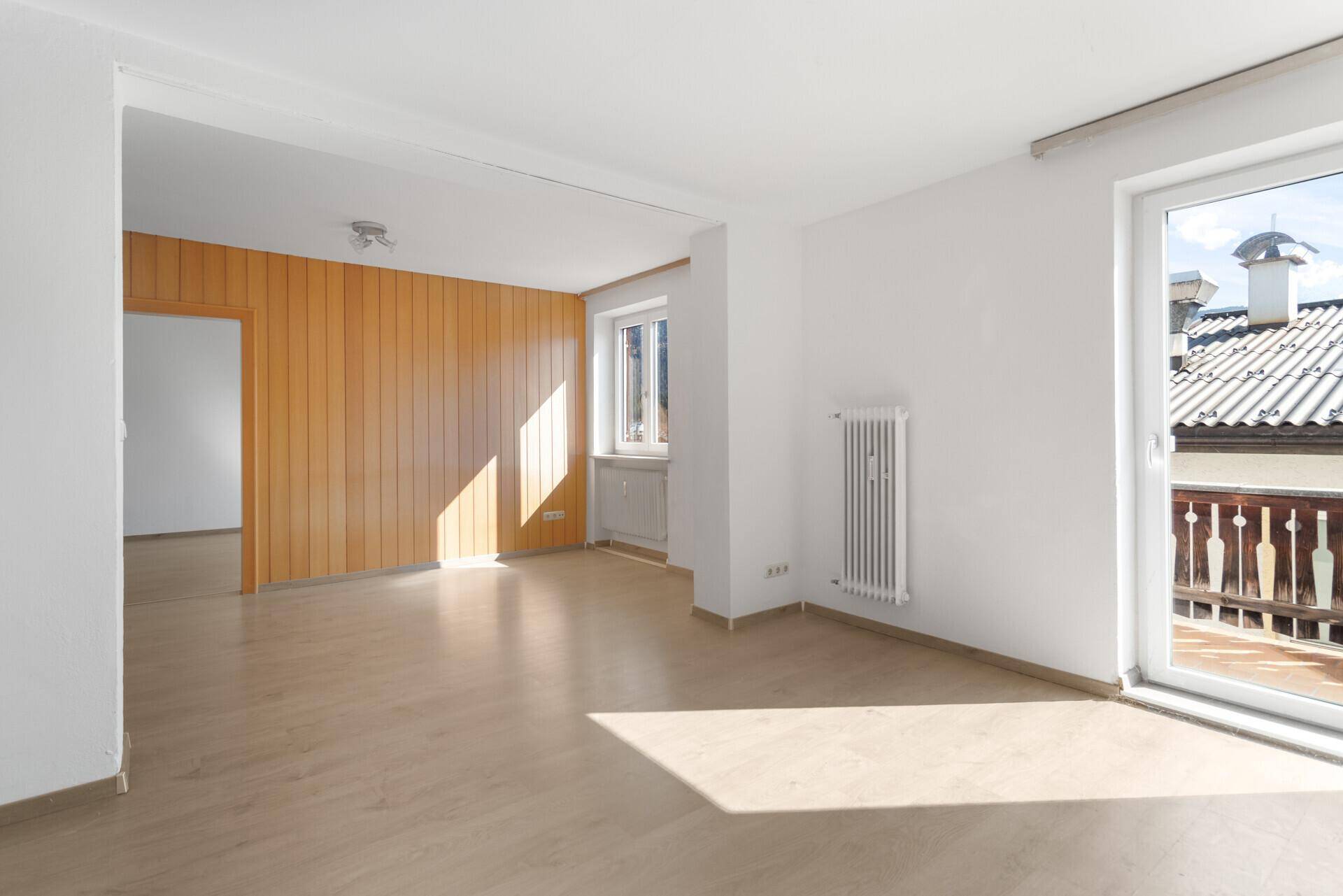 Geräumiges Zimmer mit Laminatboden, Holzvertäfelung und Balkonzugang.