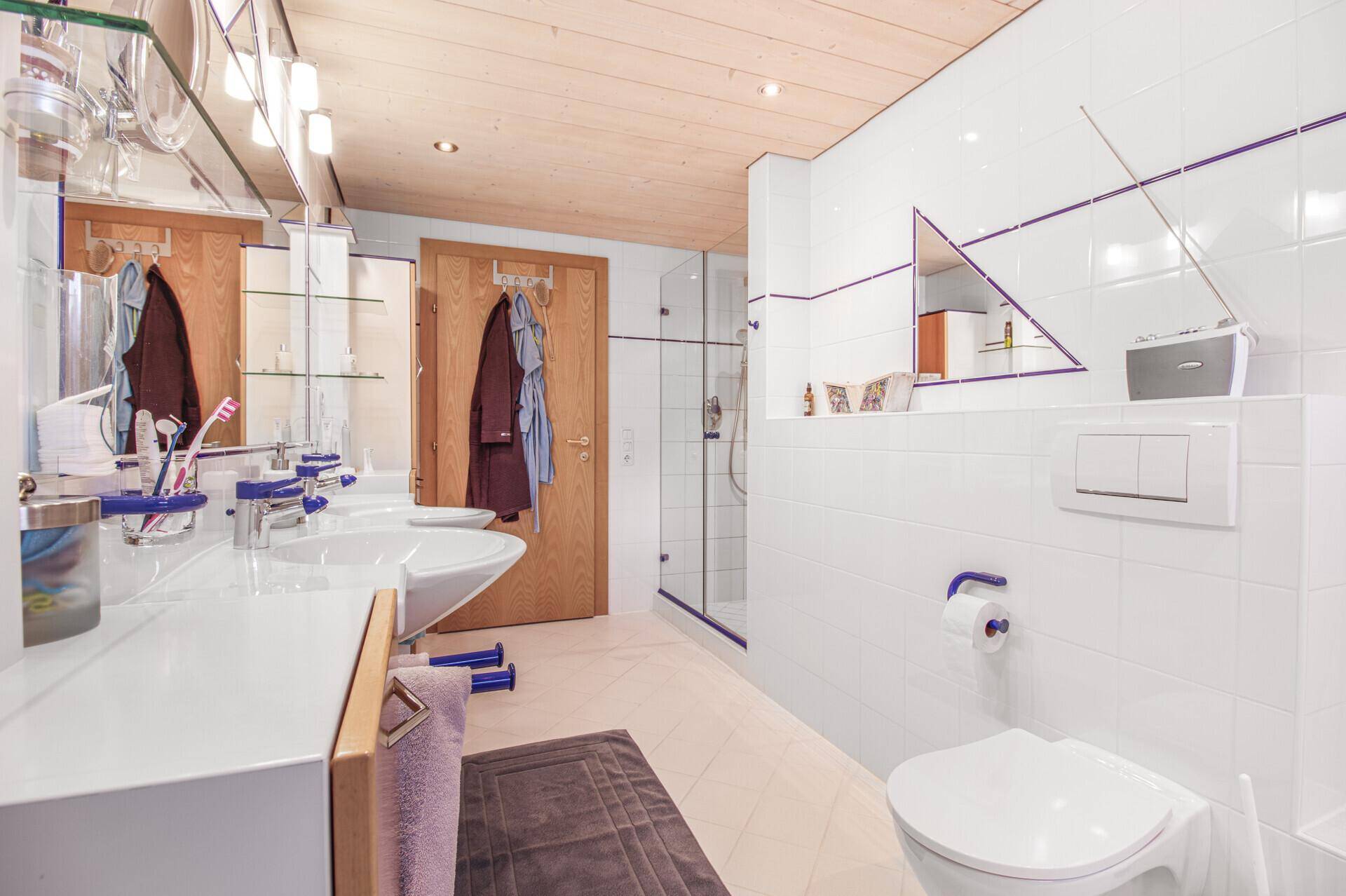 Modernes Badezimmer mit Doppelwaschbecken, Dusche und Holzbalkendecke.