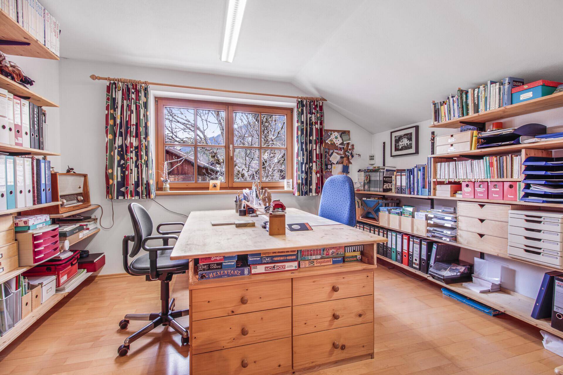 Funktionales Büro mit großem Schreibtisch, vielen Regalen und Fenster mit Bergblick.