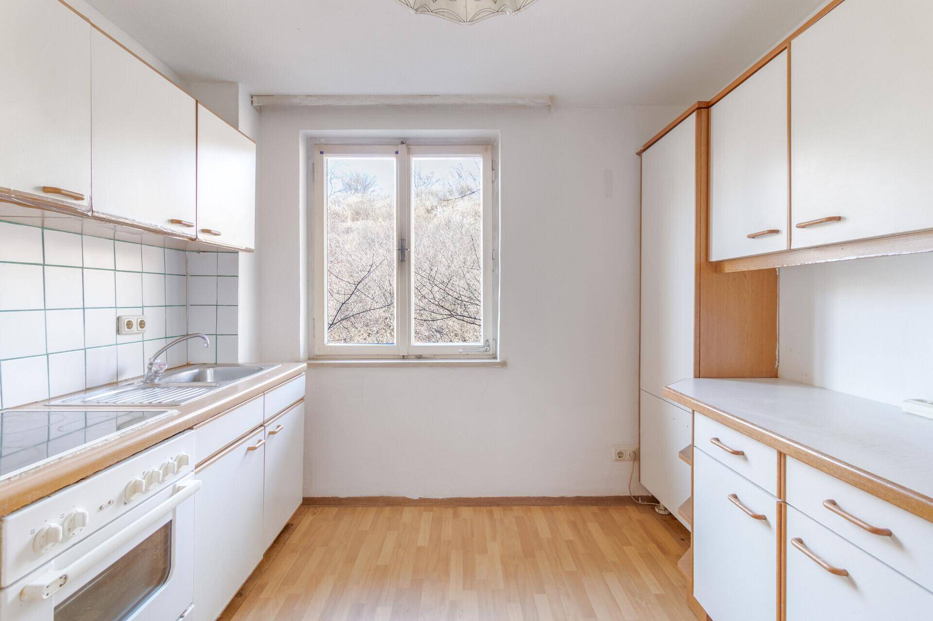 Helle Küche mit weißen Schränken, Fenster und Laminatboden.