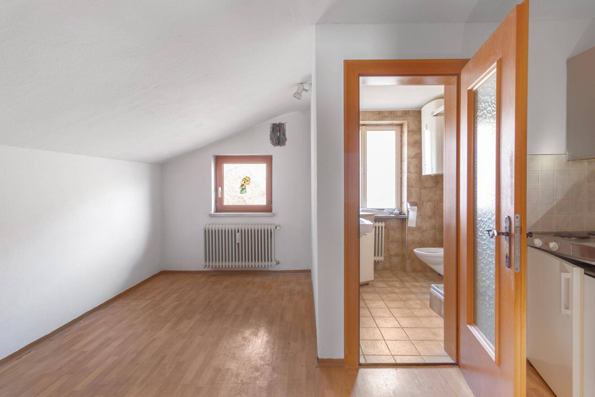 Helles Zimmer im Dachgeschoss mit Laminatboden, schräger Decke und Fenster.