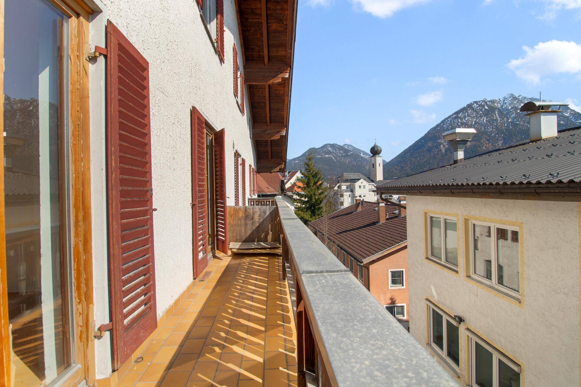 Langer Balkon mit Fliesenboden und Holzgeländer, mit Blick auf die Stadt und Berge.