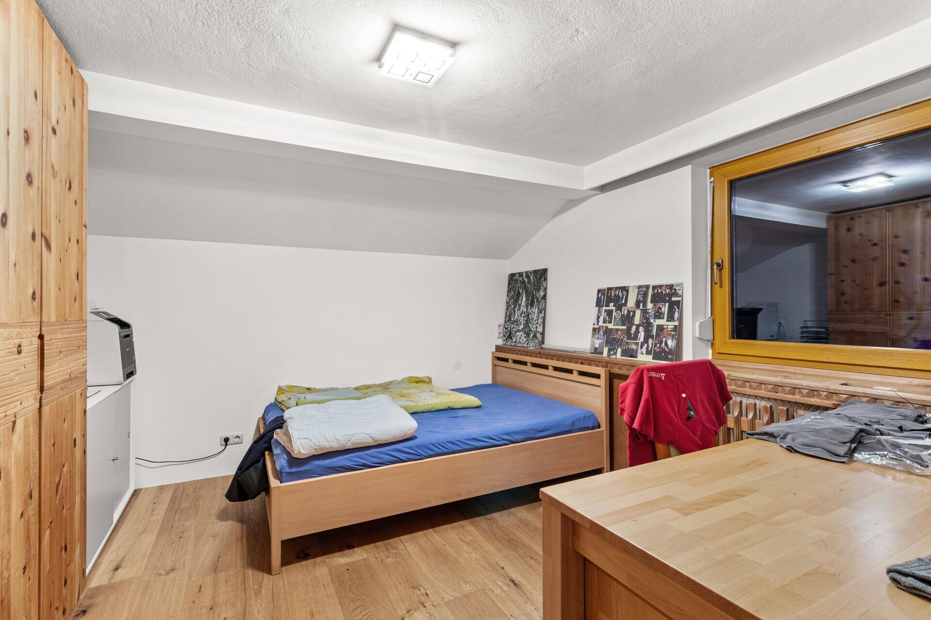 Schlafzimmer mit Holzbett, Holzboden und großem Fenster, das viel Licht hereinlässt.