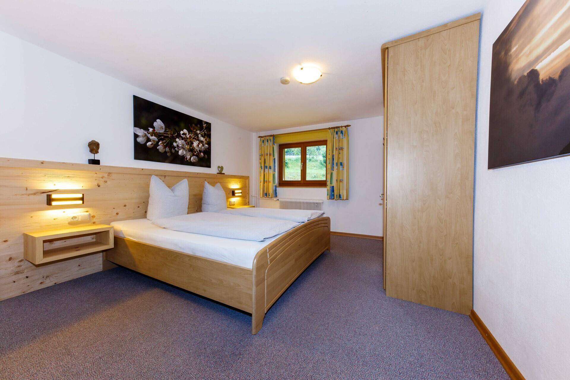 Helles Schlafzimmer mit Holzbett, Teppichboden und Fenster für Tageslicht.