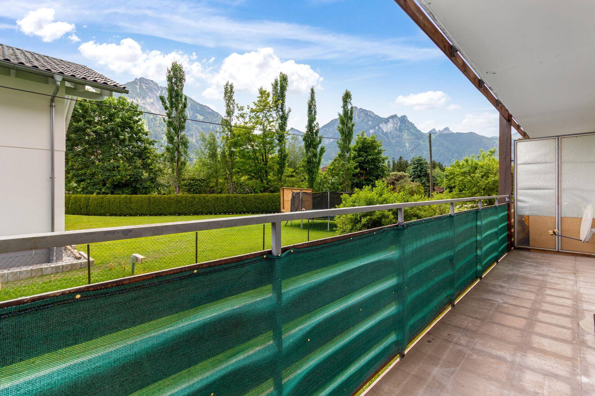 Balkon mit Bergblick, grüner Sichtschutzwand und Blick auf den Garten mit Trampolin.
