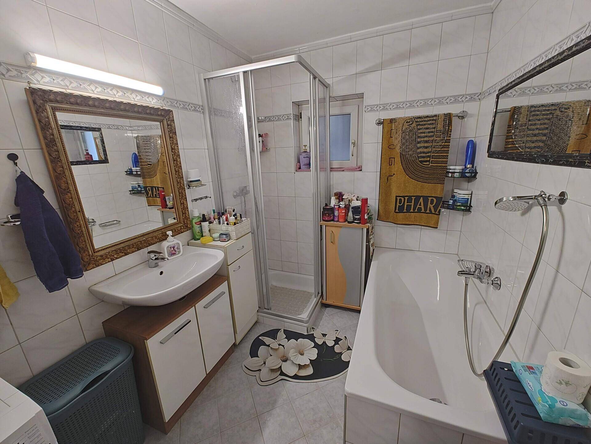 Badezimmer mit Badewanne, Dusche und großem Spiegel in Goldrahmen.