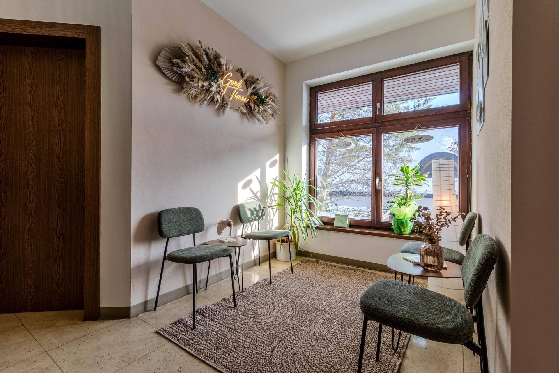 Gemütlicher Wartebereich mit modernen Stühlen, kleinen Tischen und einem großen Fenster, das viel Licht spendet.