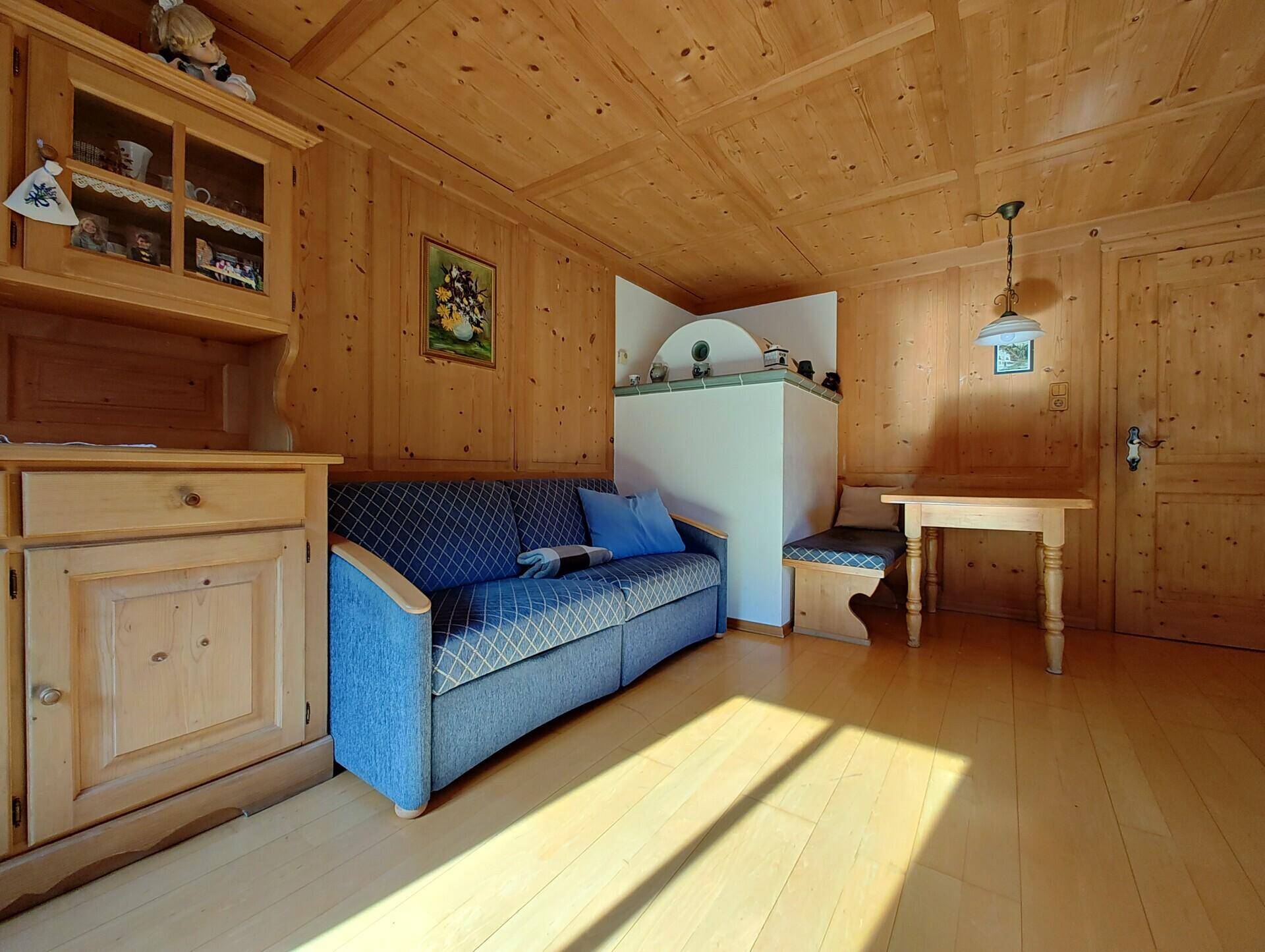 Alpines Wohnzimmer mit bequemer Couch, Kachelofen und rustikaler Holzvertäfelung.