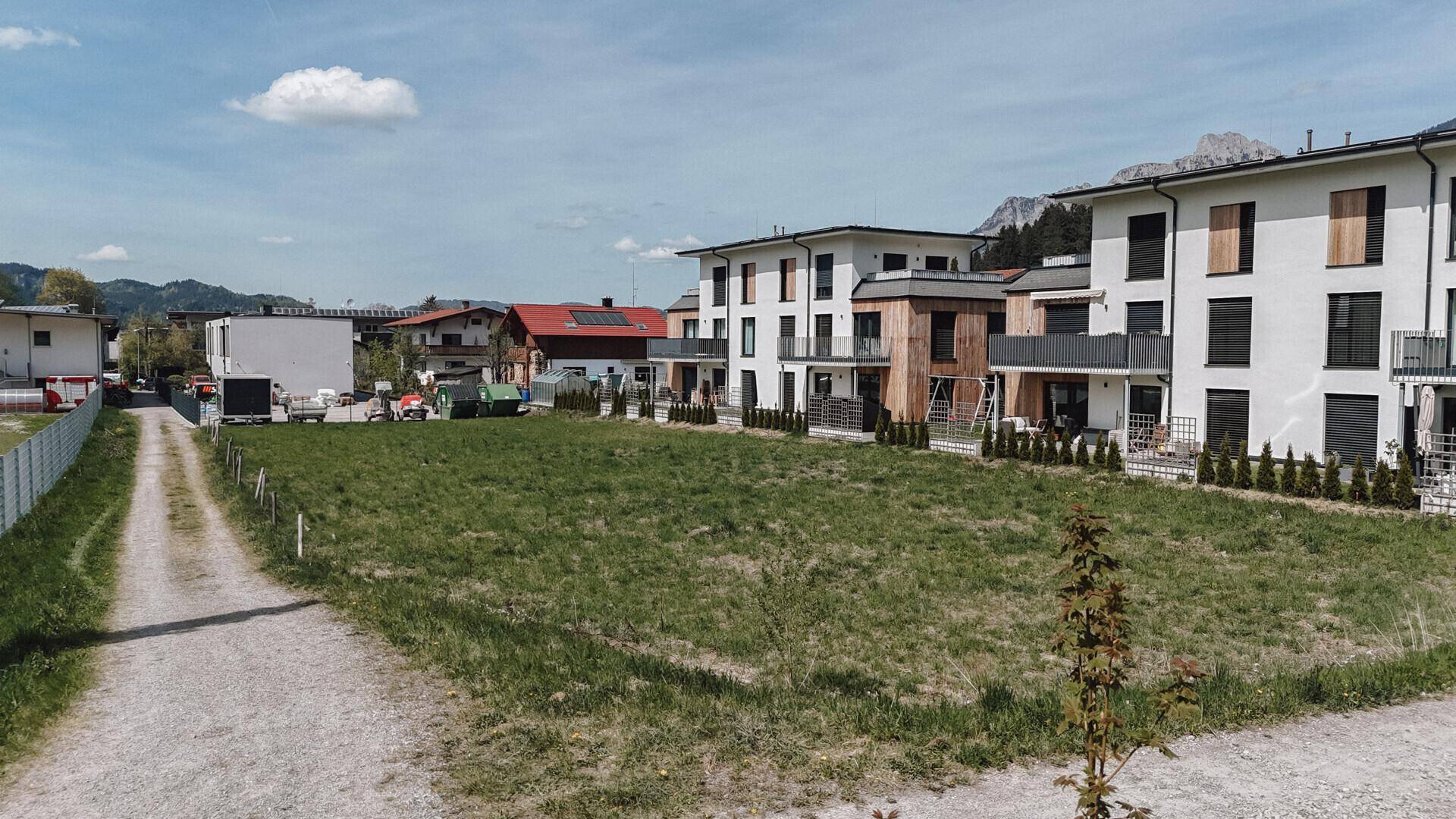 Großes, grünes Grundstück mit modernen Gebäuden auf der rechten Seite und einer beeindruckenden Bergkulisse im Hintergrund.