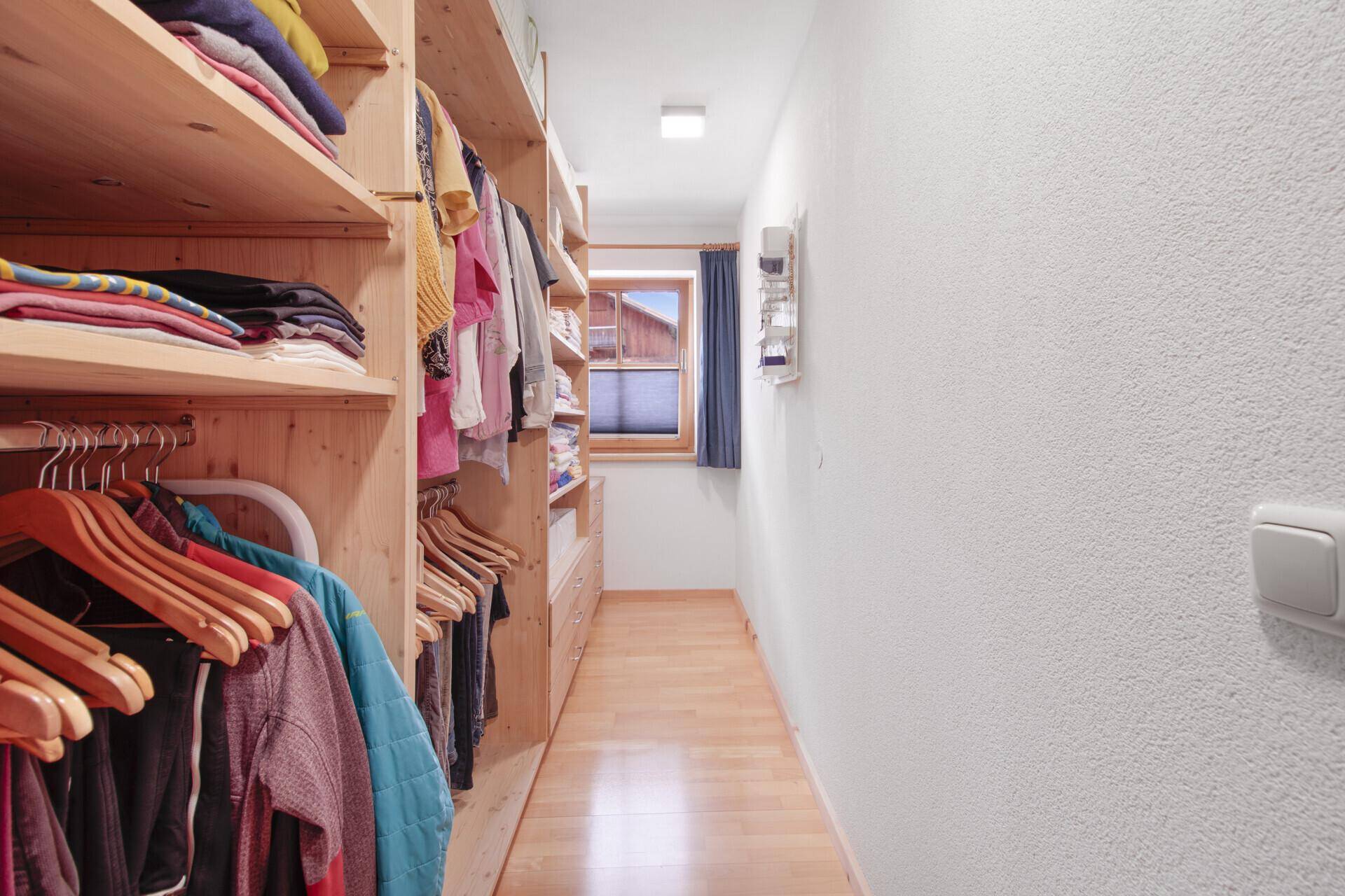 Praktischer begehbarer Kleiderschrank mit Holzregalen und Fenster für Tageslicht.