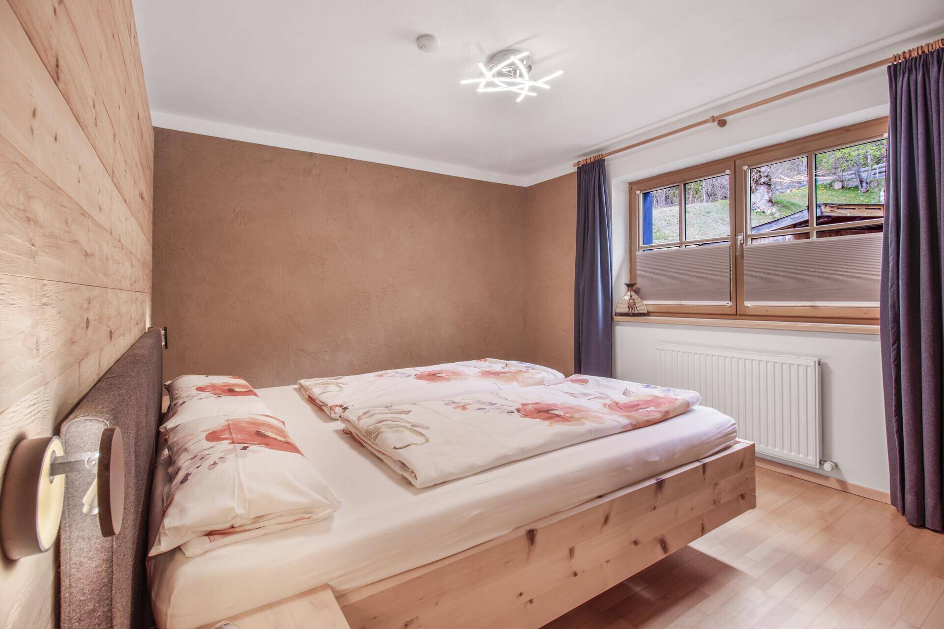 Gemütliches Schlafzimmer mit Holzbett, Holzvertäfelung und Fensterblick ins Grüne.