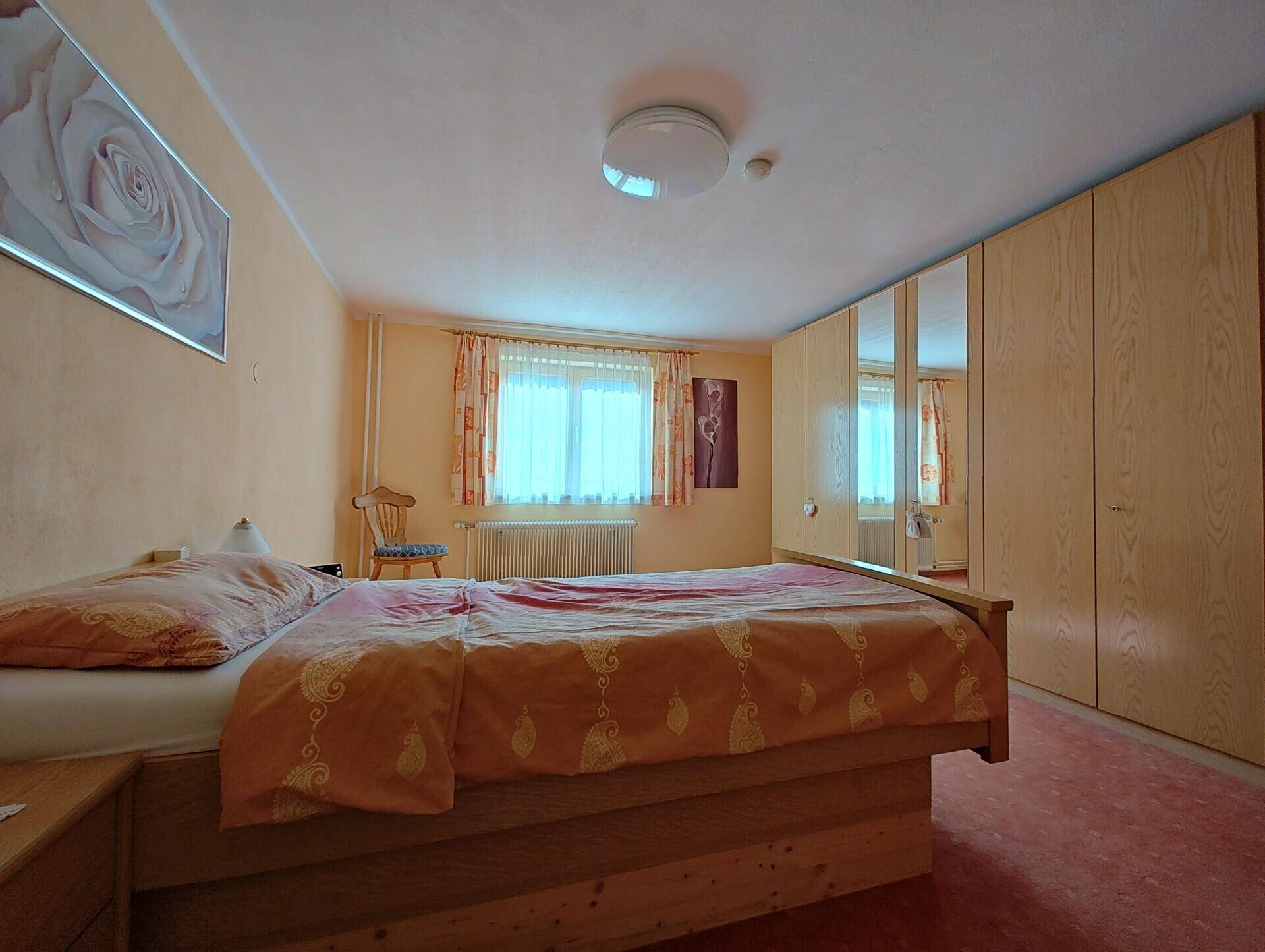 Geräumiges Schlafzimmer mit Holzbett, großem Spiegelschrank und warmen orangefarbenen Wänden.
