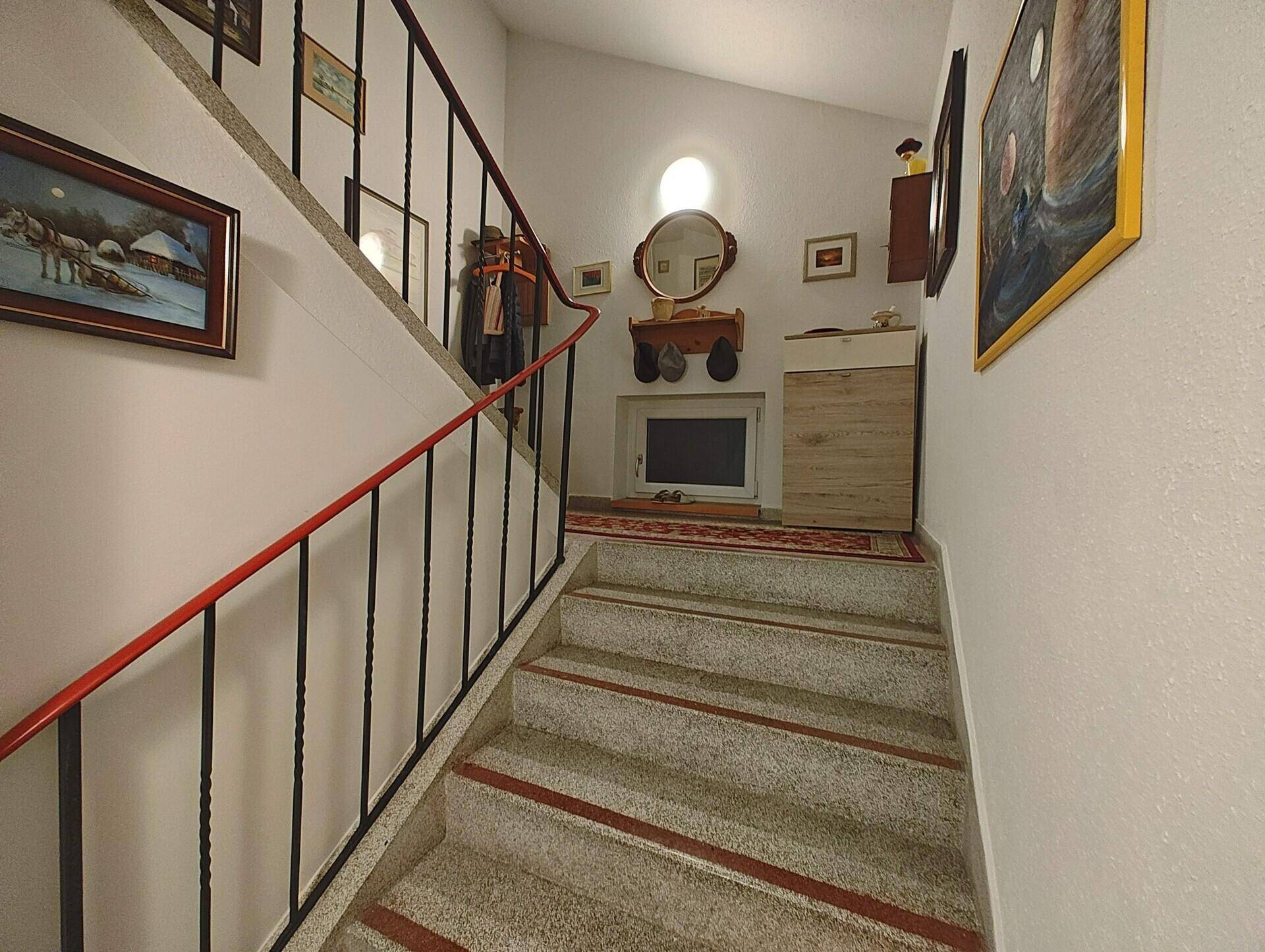 Treppenhaus mit rotem Handlauf und Bildern an der Wand.