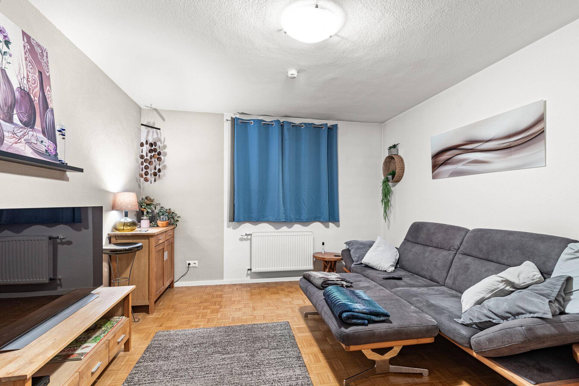 Gemütliches Wohnzimmer mit großem Sofa, Holzboden und blauen Vorhängen.