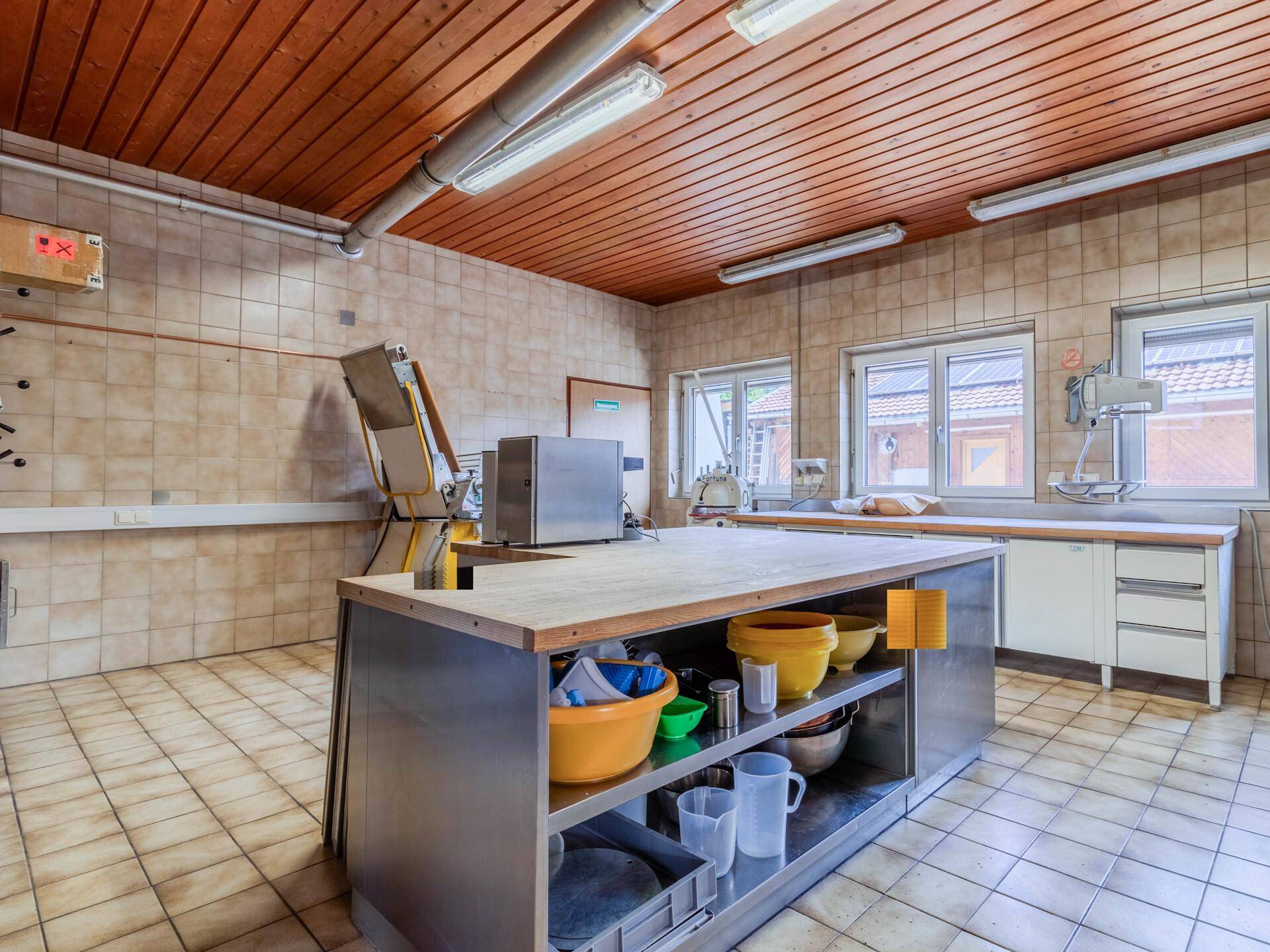 Eine geräumige Gewerbeküche mit Edelstahl-Arbeitsinsel, gefliesten Wänden und Decken aus Holzpaneelen.
