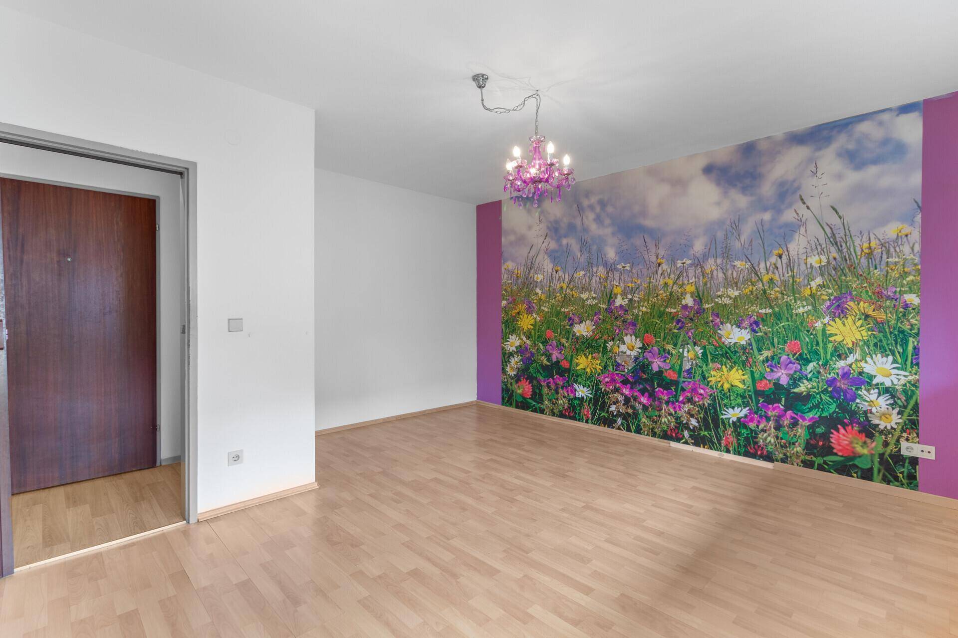 Heller Wohnbereich mit auffälliger Blumenwandtapete, Holzboden und dunkler Eingangstür.