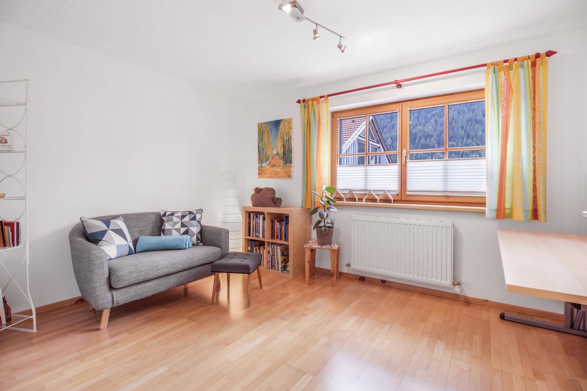 Heller Wohnraum mit bequemer Couch, Holzboden und Fenster mit Blick ins Grüne.