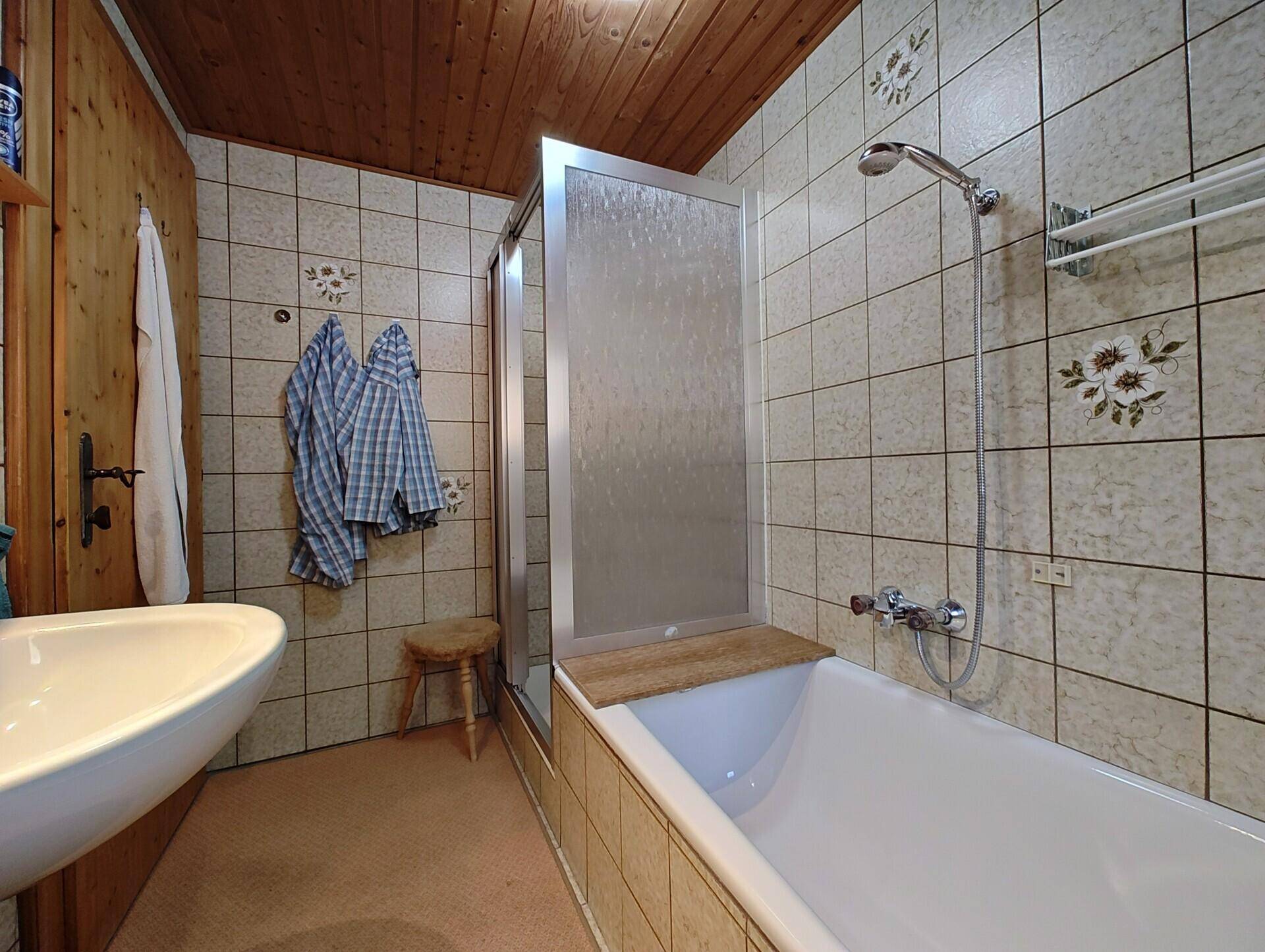 Helles Badezimmer mit Badewanne, Duschabtrennung und Holzdecke.