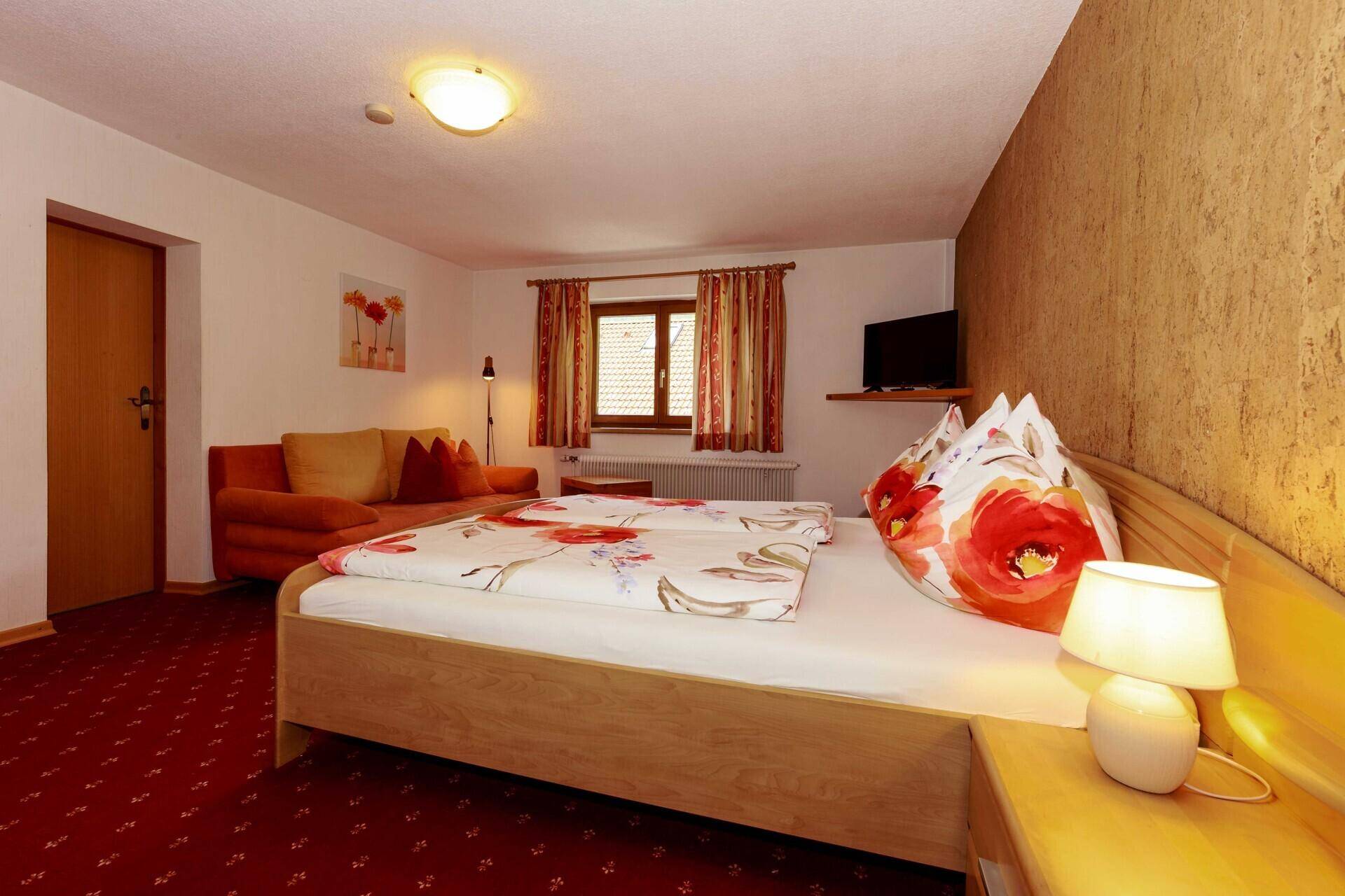 Helles Schlafzimmer mit Holzbett, Sofa und rotem Teppichboden.