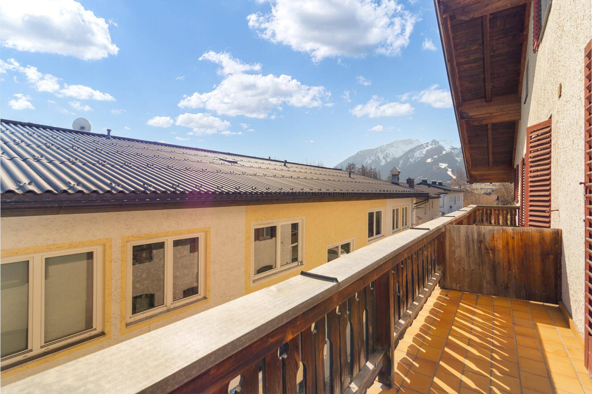 Balkon mit Fliesenboden und Holzgeländer, bietet einen Blick über die Dächer und Berge.