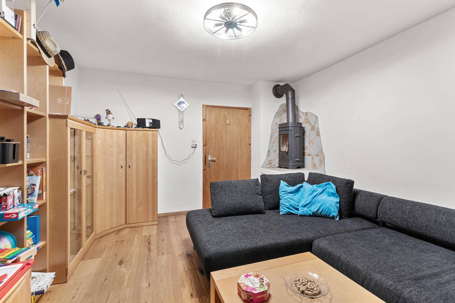 Wohnzimmer mit Kaminofen, Ecksofa und Holzmöbeln, das eine gemütliche Atmosphäre schafft.