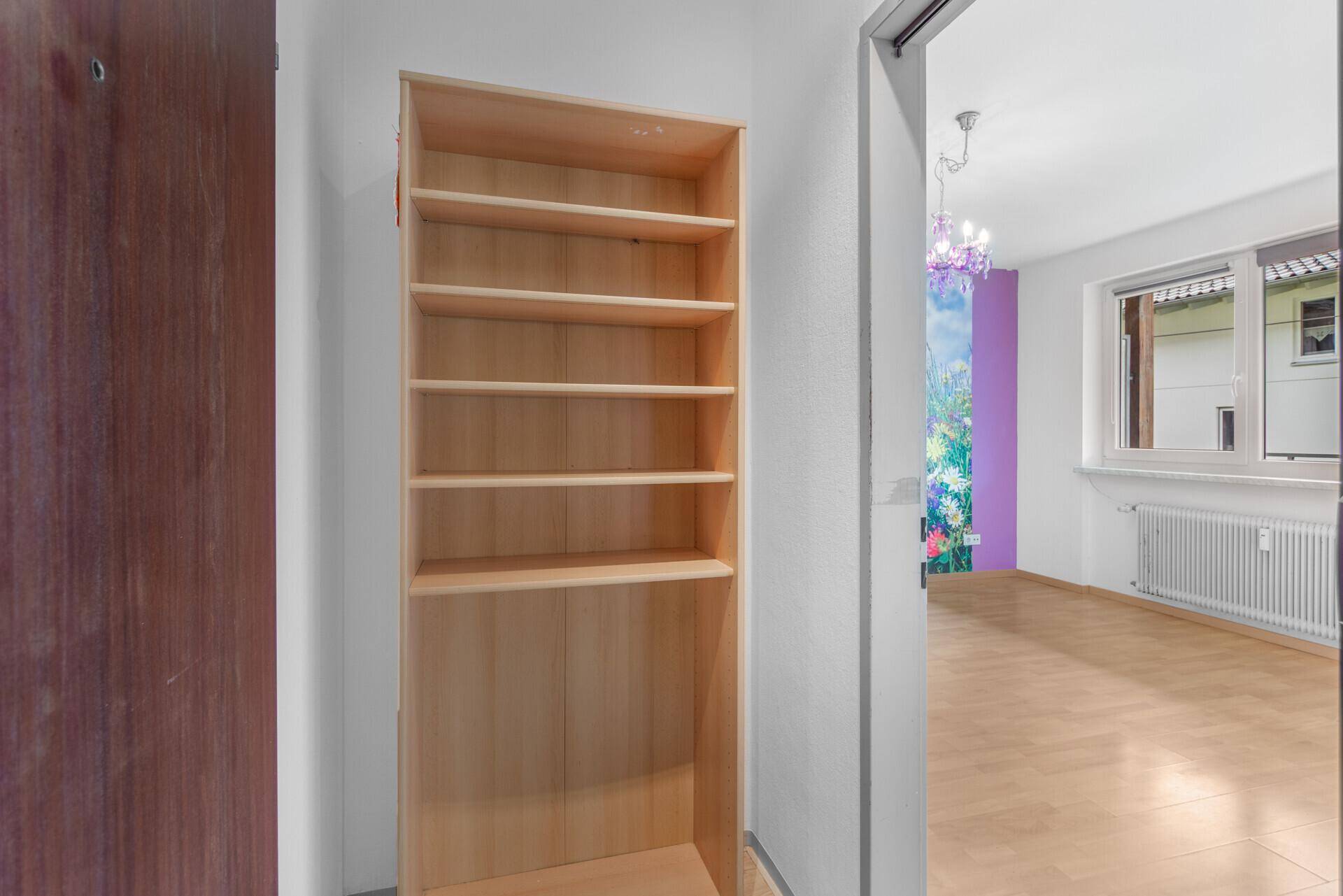 Heller Flurbereich mit Holzregal und Durchgang zum Wohnzimmer.