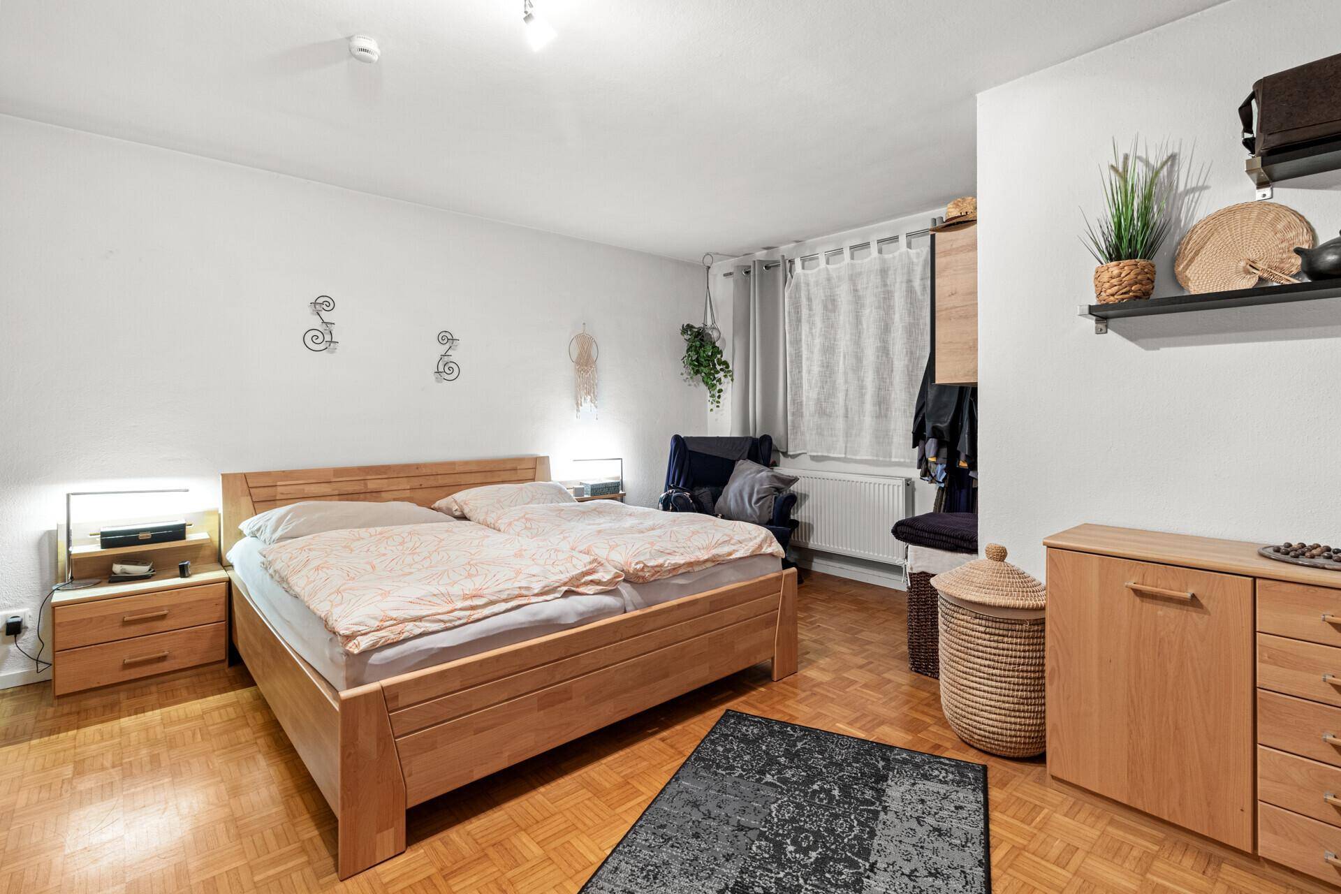 Helles Schlafzimmer mit Doppelbett, Holzmöbeln und Parkettboden.