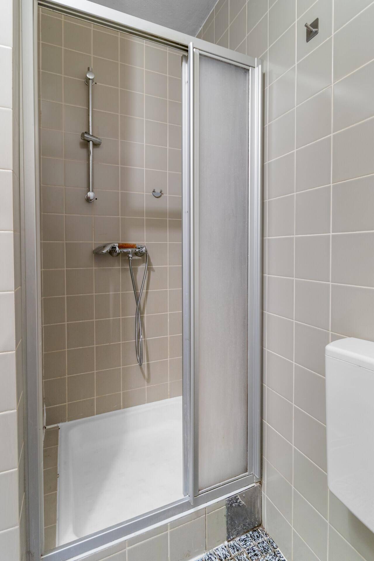 Duschkabine mit Glasschiebetür und beigefarbenen Wandfliesen im Badezimmer.