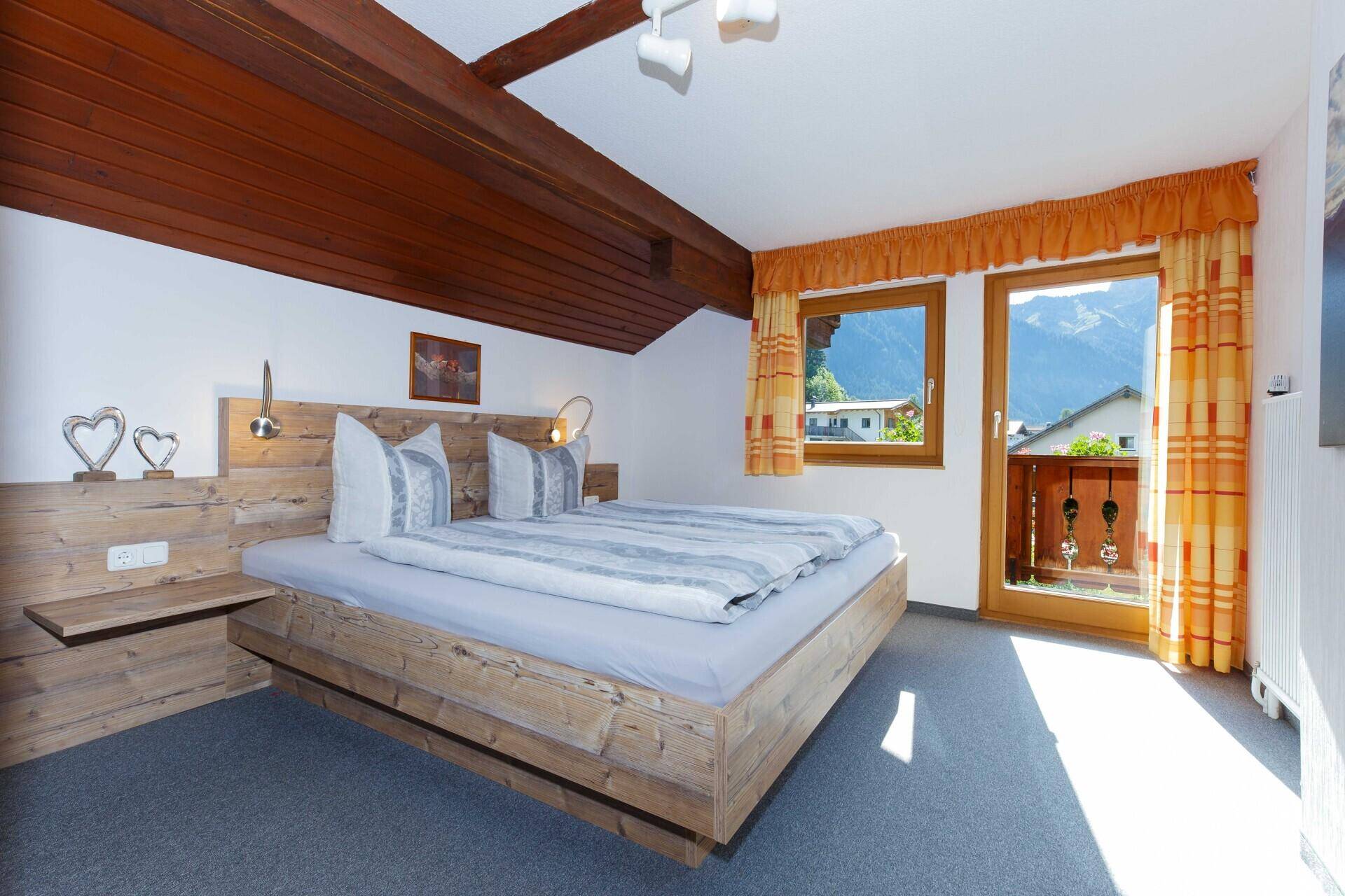 Gemütliches Schlafzimmer mit Holzbett, sichtbaren Holzbalken und Balkonzugang mit Bergblick.